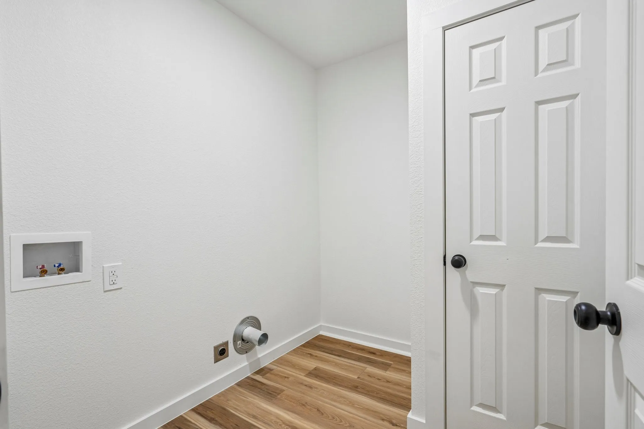 Laundry area with wood-finish flooring and white walls