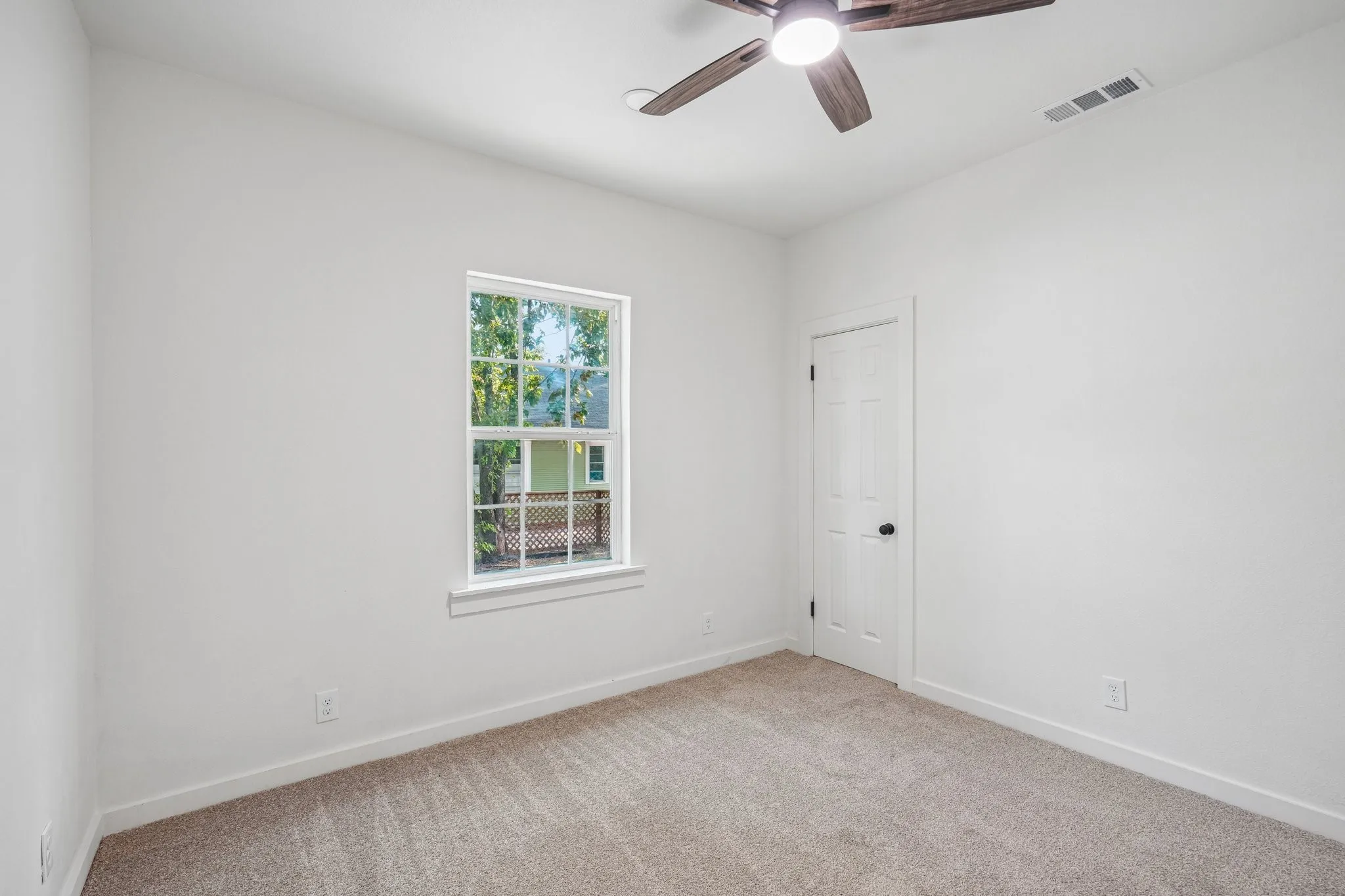 Bright interior with neutral carpet flooring, a window with exterior visibility, a ceiling fan, and a paneled door