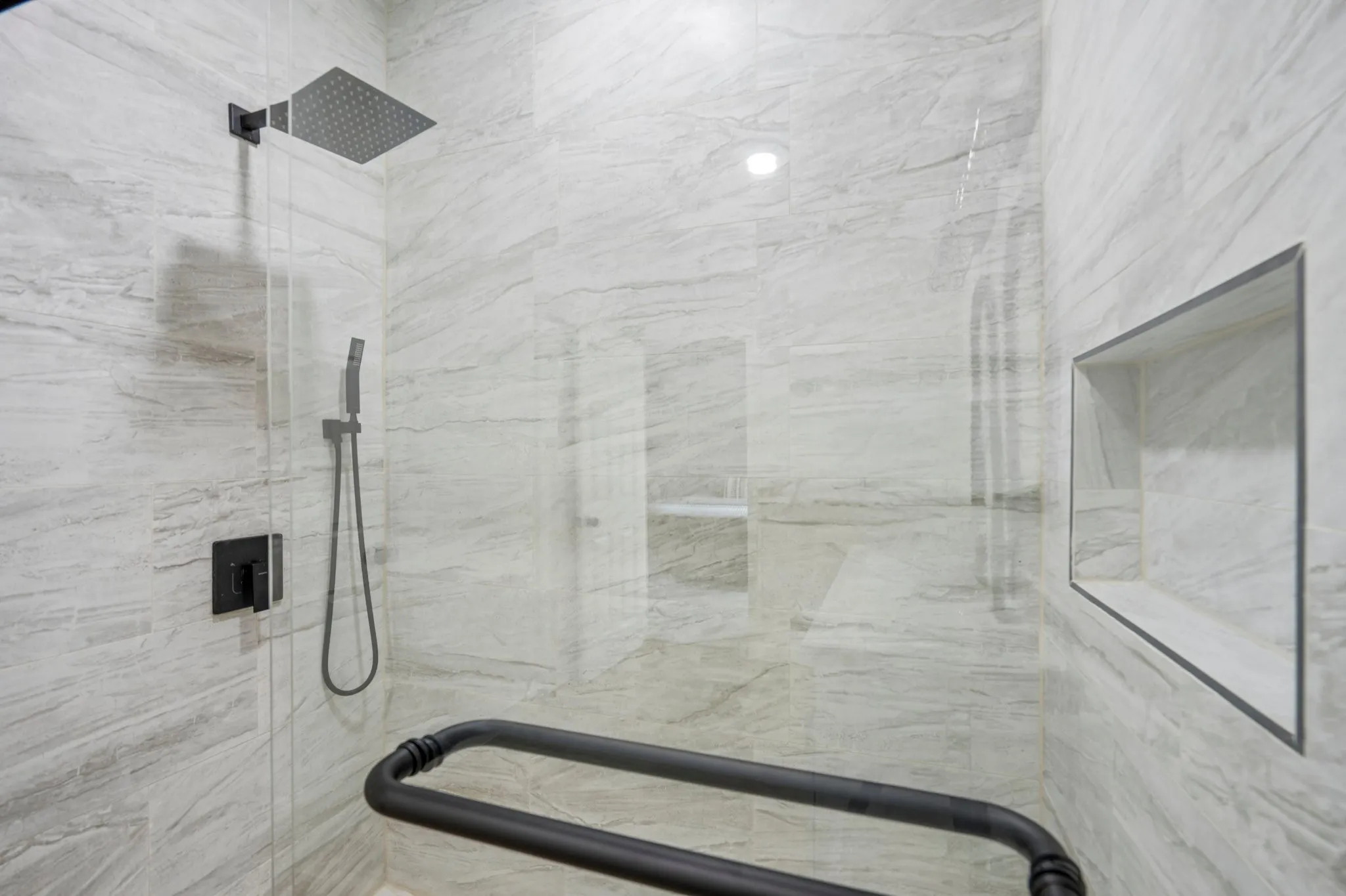 Walk-in shower with full-height tile surround, a built-in shower niche, and a matte black rain shower head and hand-held shower fixture