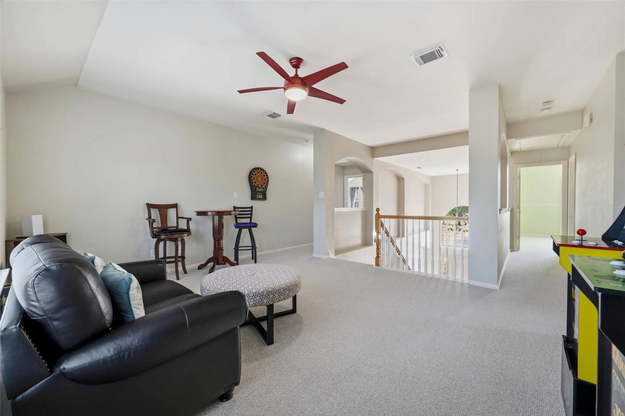 Vaulted ceiling with a ceiling fan, carpet flooring, wood railing, and an arched doorway