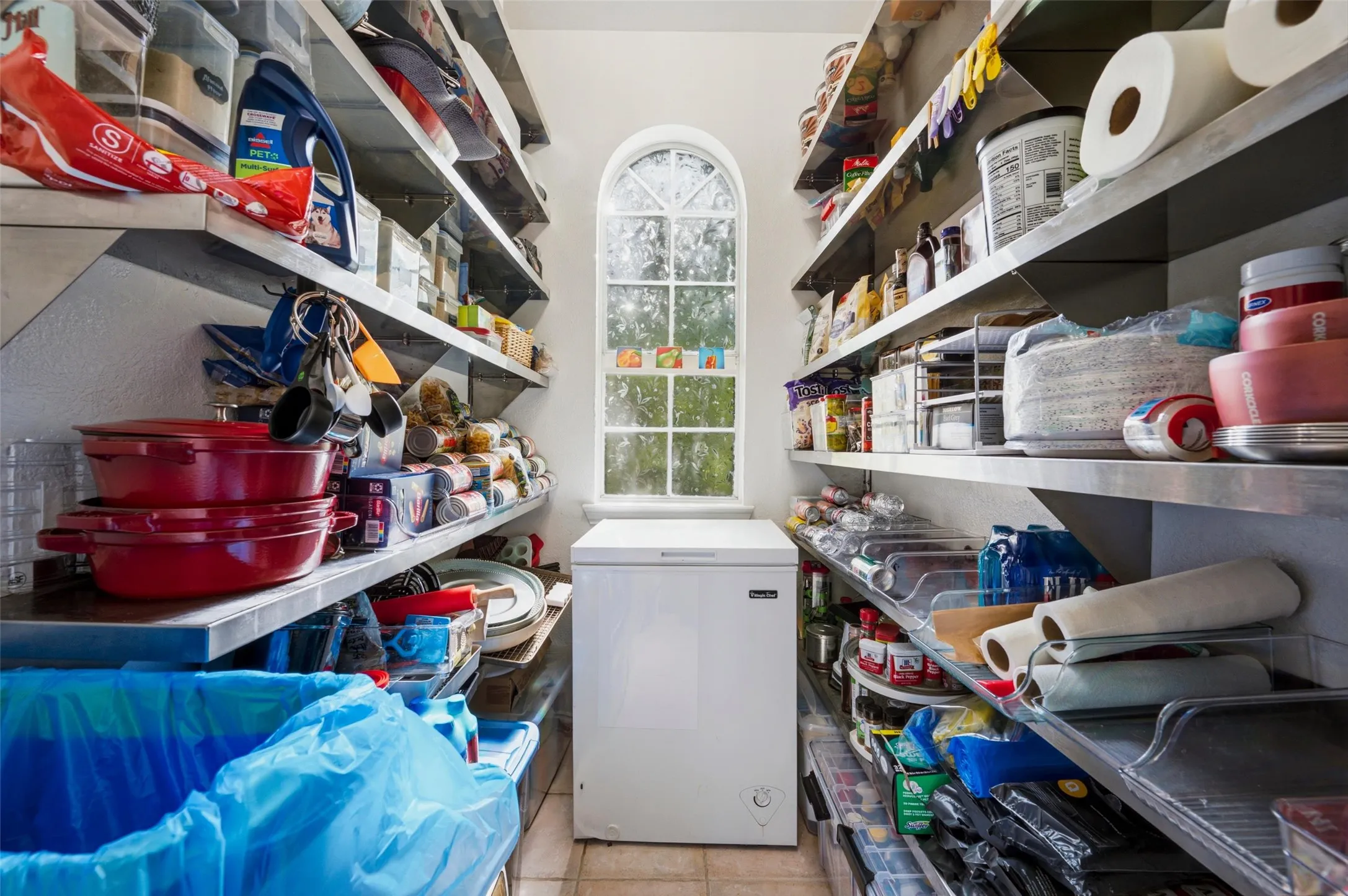Pantry featuring extensive stainless steel shelving, arched window, and tiled flooring