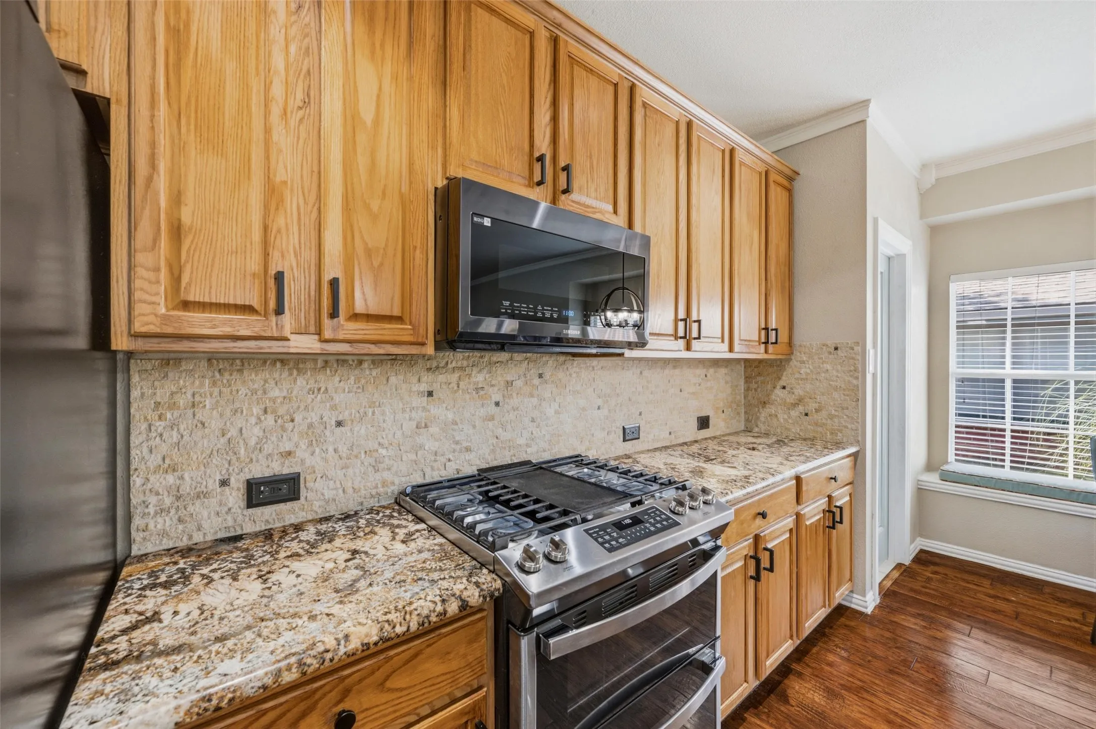 Wood-finish cabinetry with dark hardware, stone slab countertops, stone tile backsplash, stainless steel range with double oven, and a built-in microwave