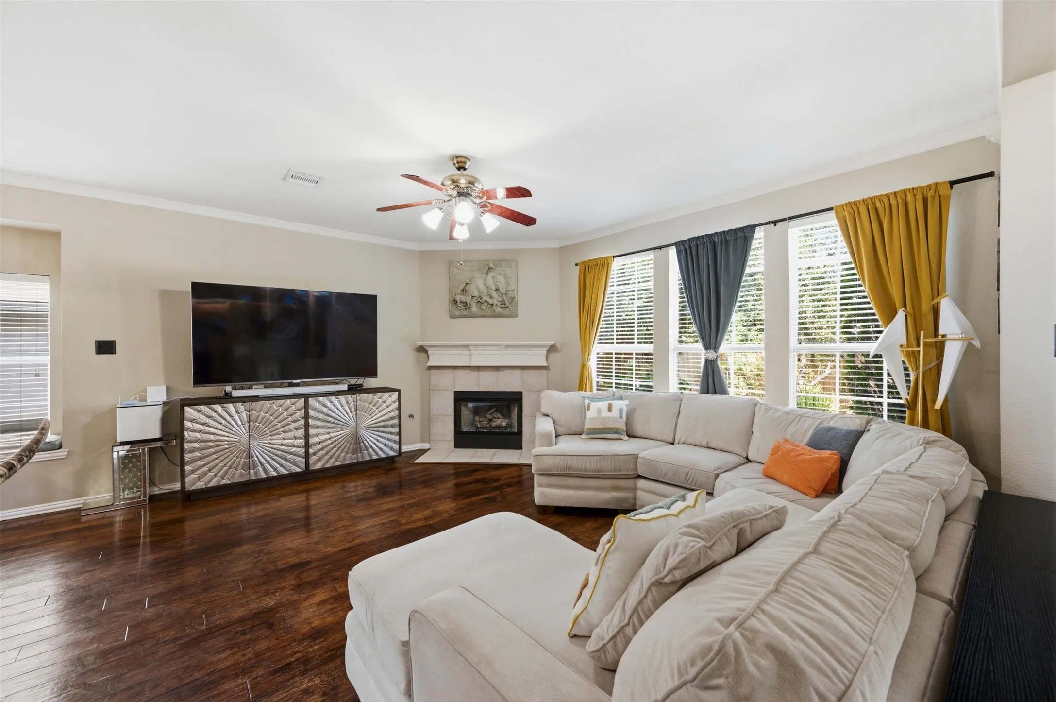 Hardwood flooring, corner fireplace with mantel, multiple large windows, ceiling fan, and crown molding