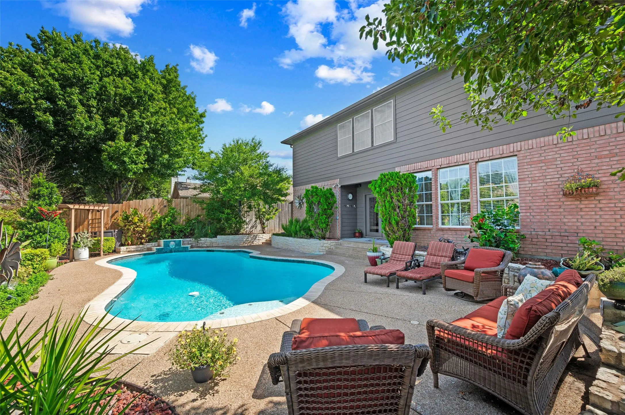 Outdoor swimming pool with integrated spa and rock-finish water feature, surrounded by a concrete patio
