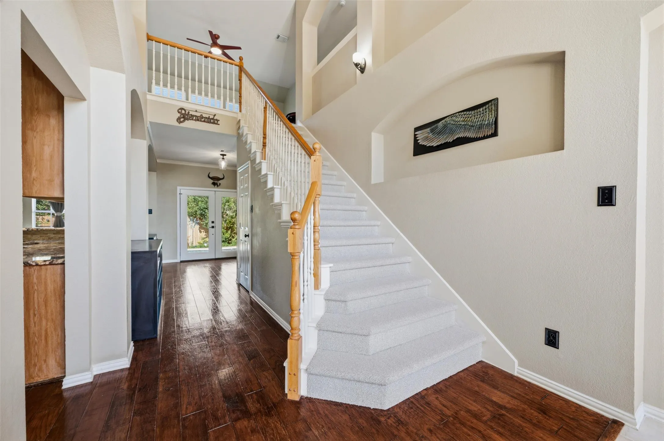 Two-story foyer with rich wood-finish flooring, a carpeted staircase with wood and white balusters, and a recessed wall niche