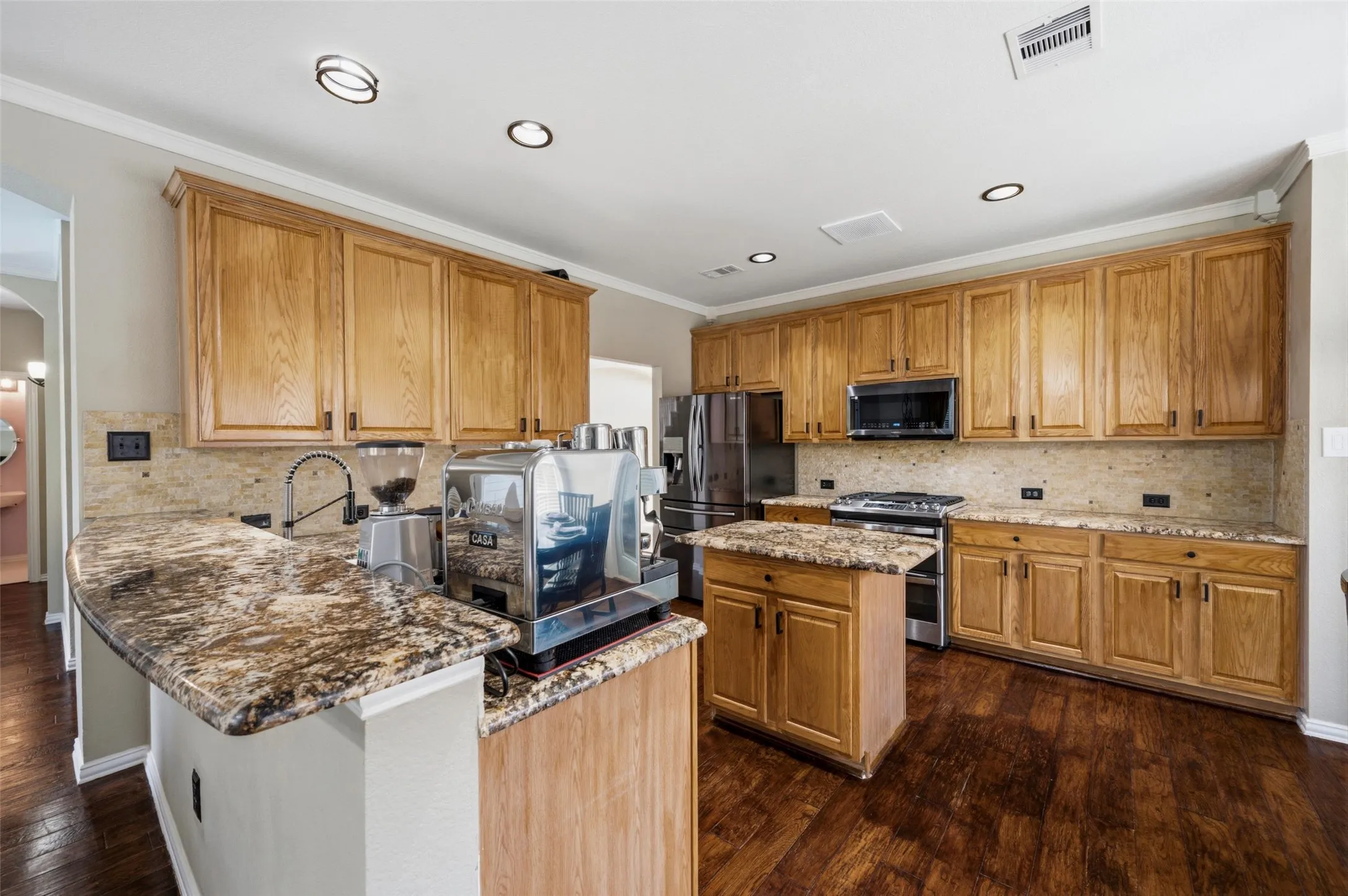 Kitchen featuring warm-toned wood cabinetry, stone countertops, a tile backsplash, and stainless steel appliances