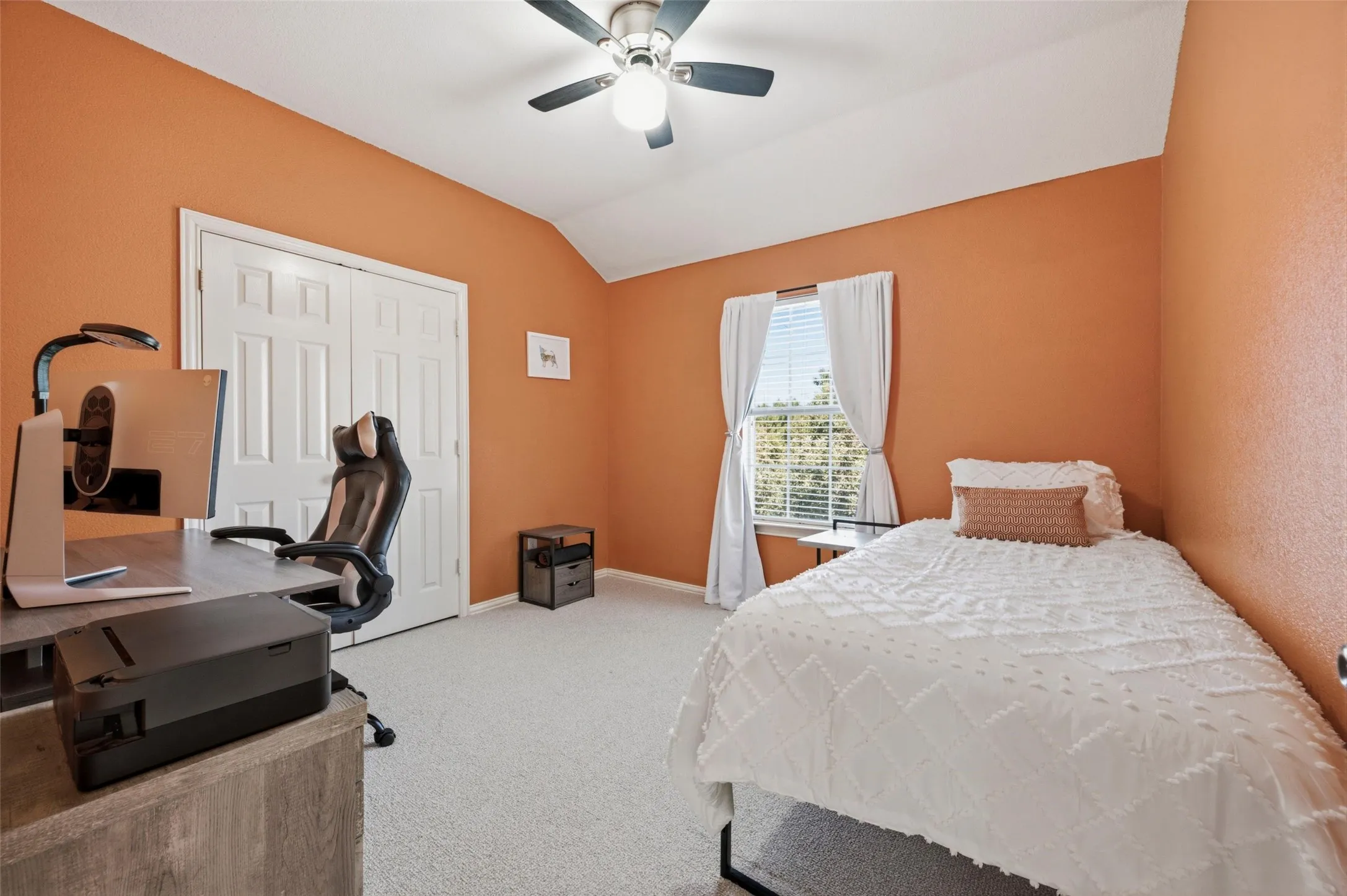Vaulted ceiling, ceiling fan, double pane window, wood-finish desk, and light-colored carpet