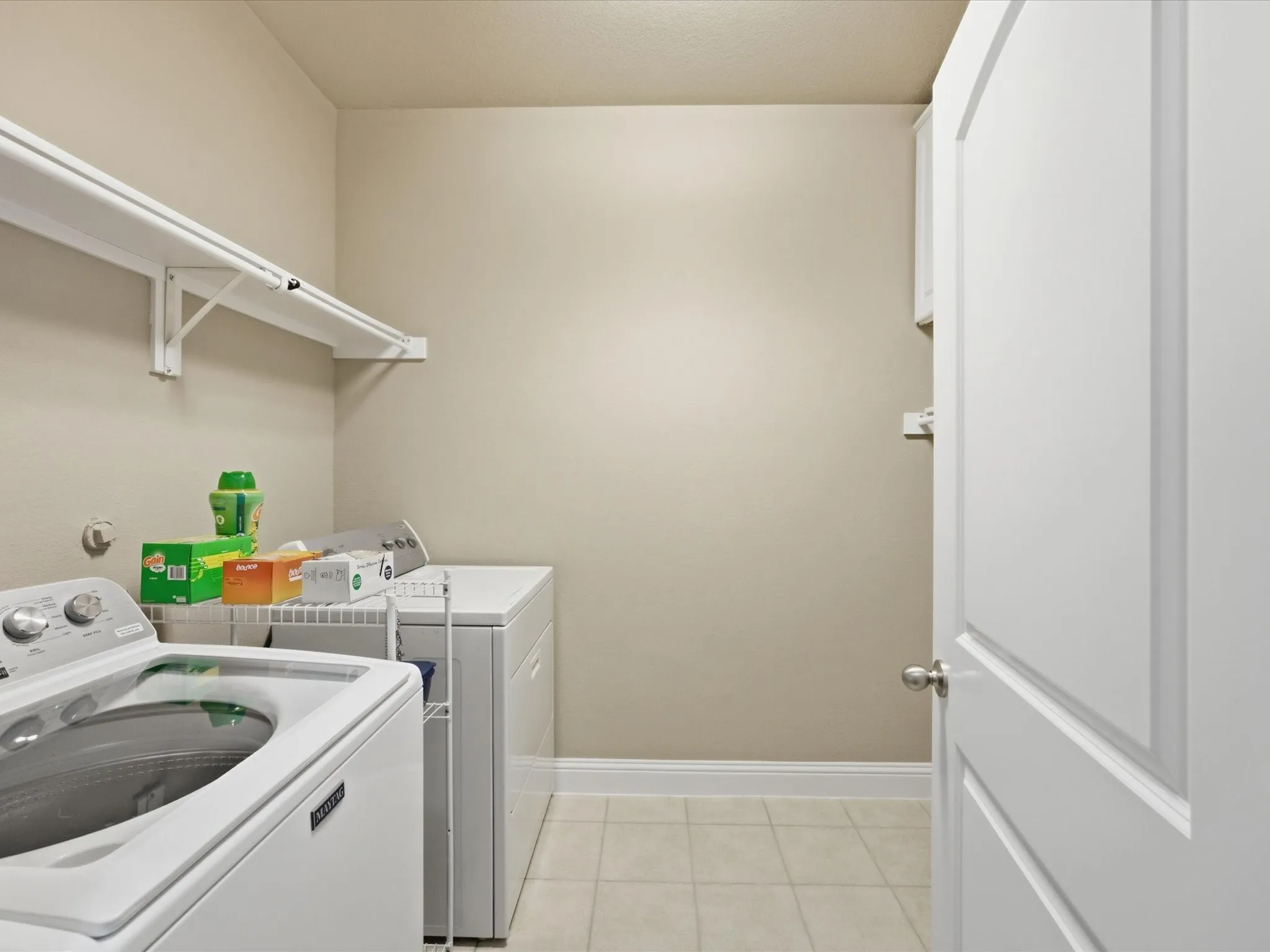 Laundry space featuring white shelving, light-toned wall paint, and tiled flooring