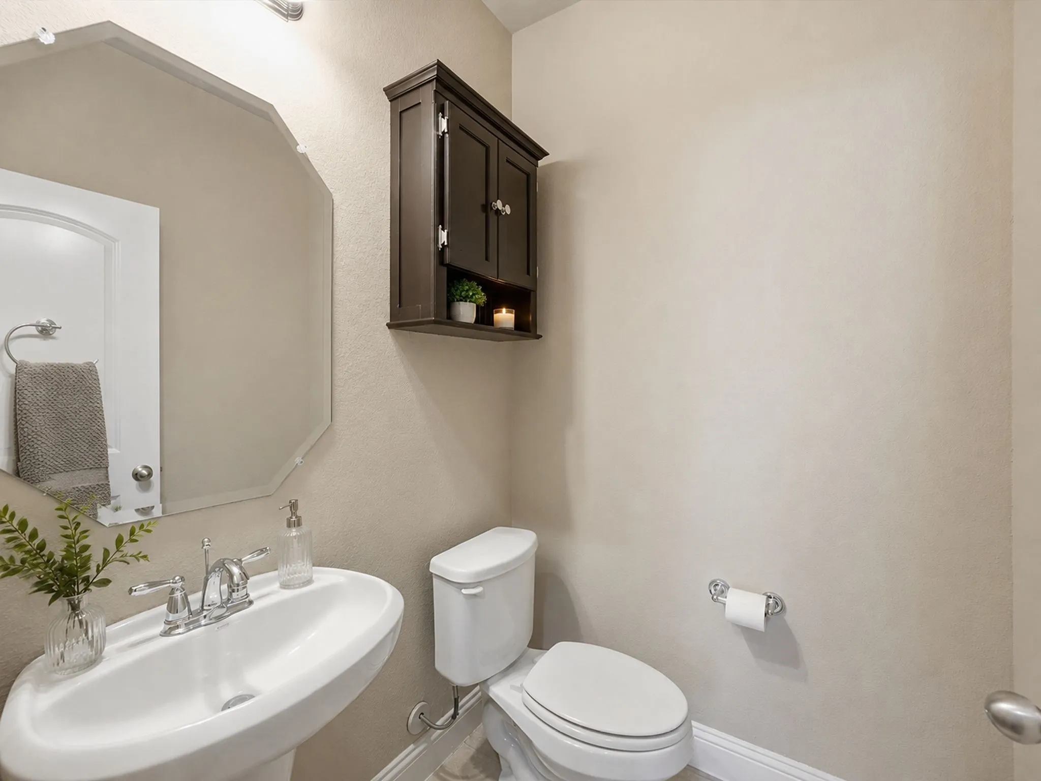 Pedestal sink with chrome faucet, octagonal mirror, wall-mounted dark wood cabinetry, white toilet, and neutral wall tones