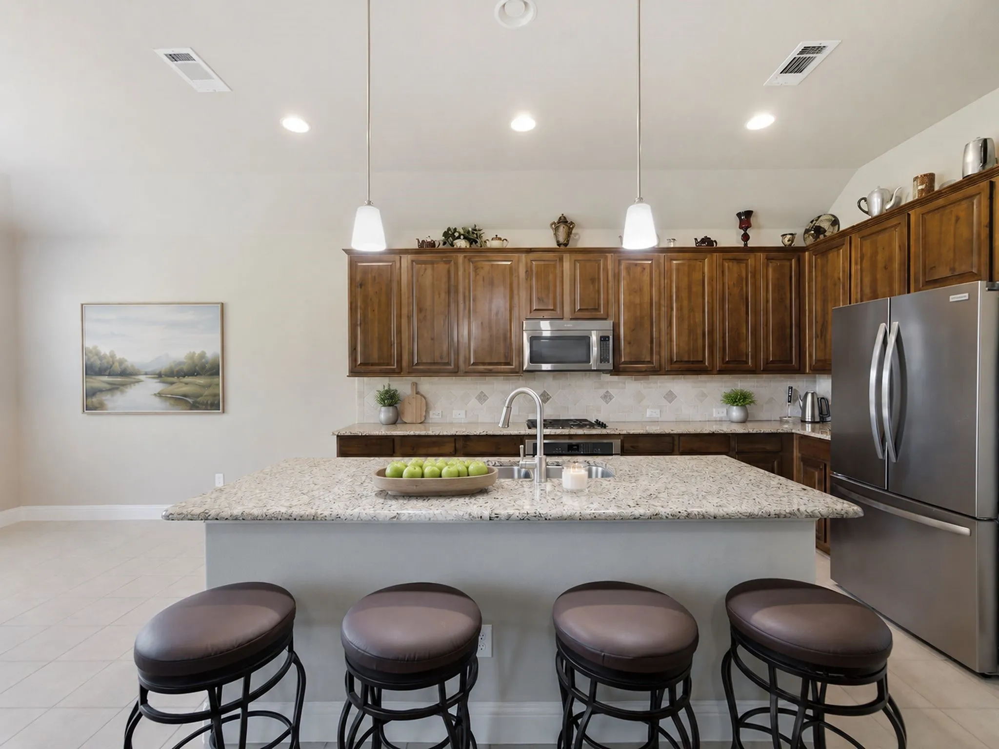 Kitchen featuring an expansive island with a light-toned countertop, wood-finish cabinetry, stainless steel appliances, and recessed lighting with pendant fixtures