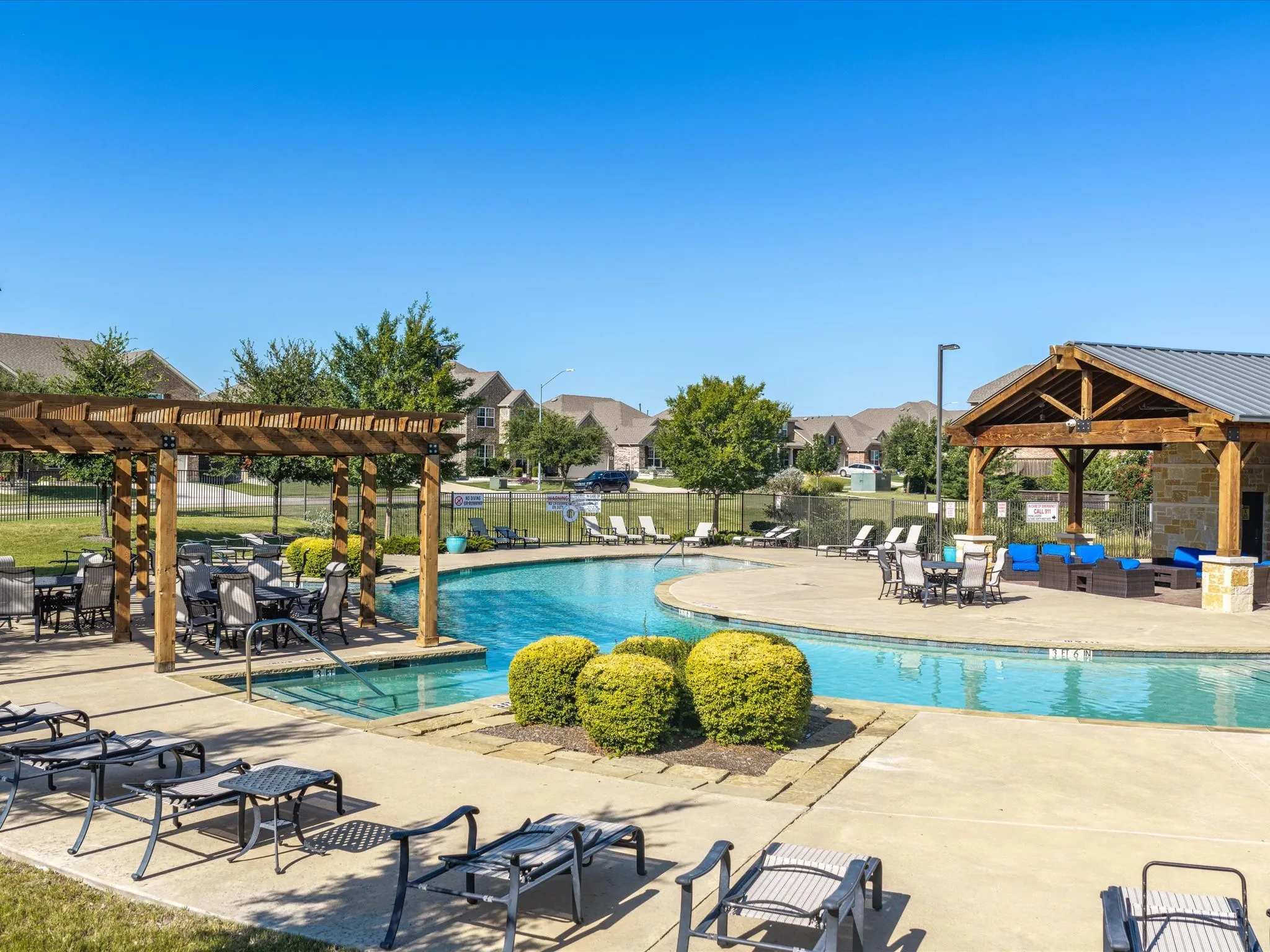 Expansive swimming pool with concrete decking, a wooden pergola, and a covered pavilion with stone accents