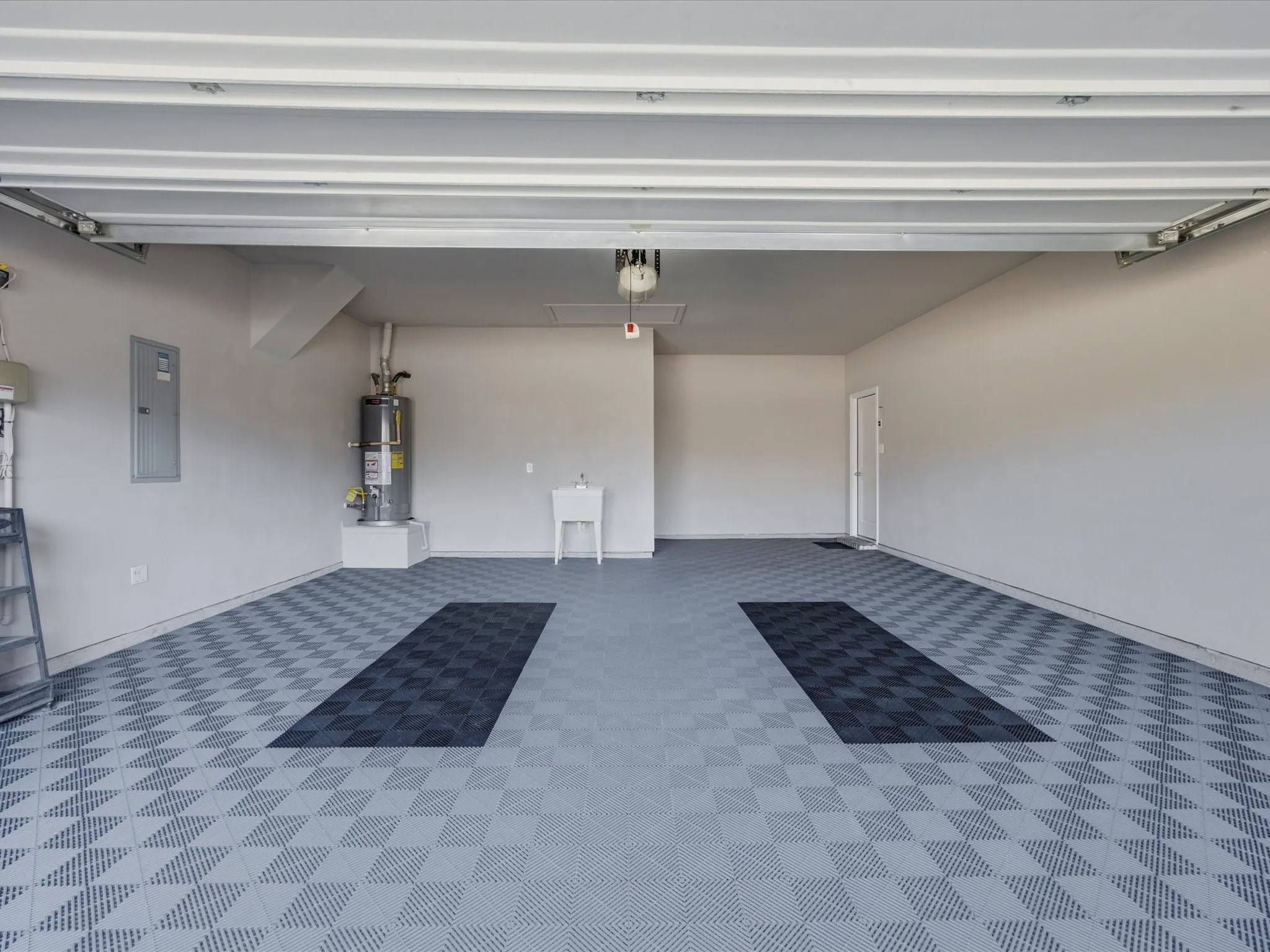 Garage featuring checkered floor tiles, a utility sink, and a water heater