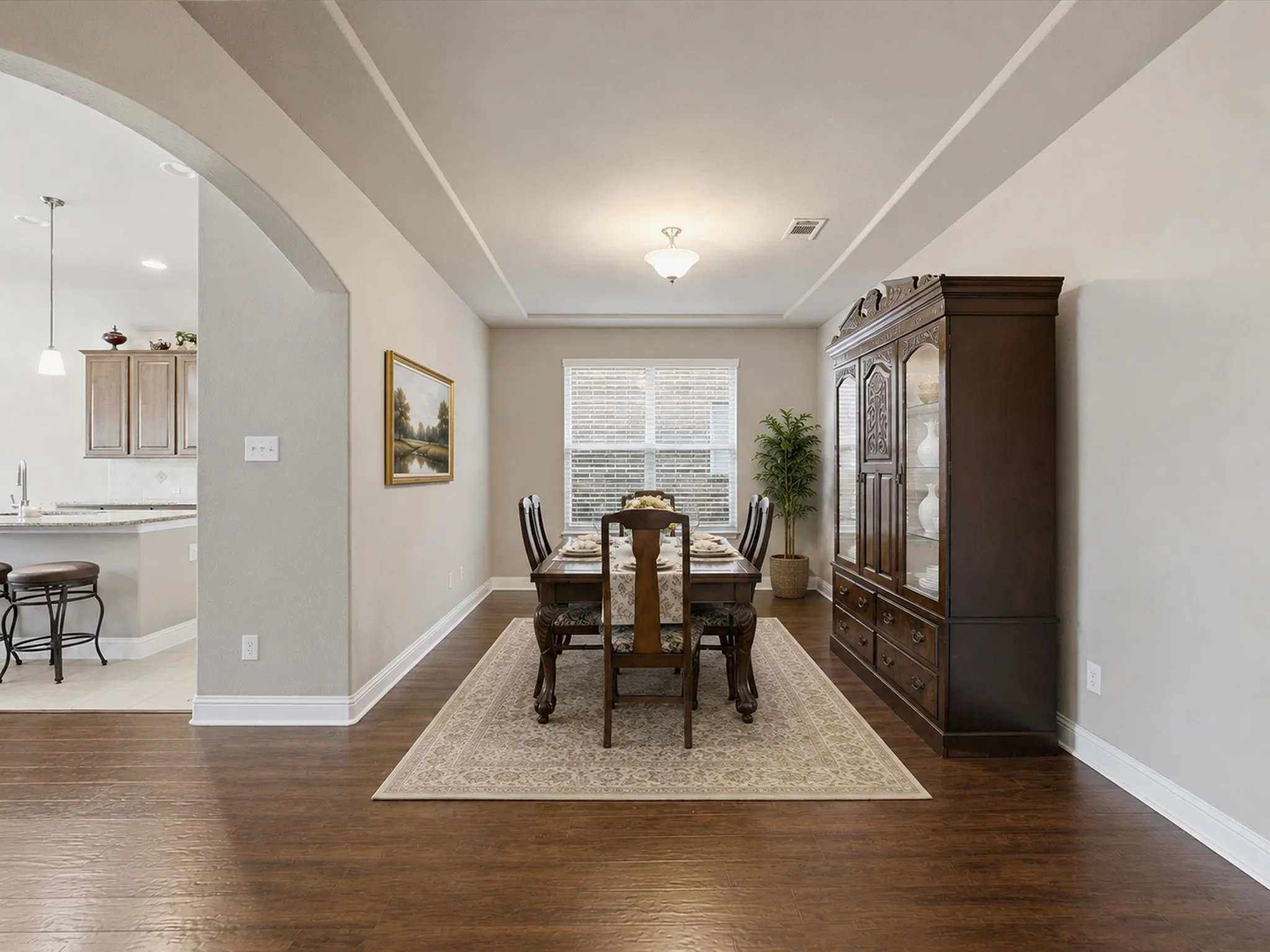 Wood-finish flooring, recessed ceiling with a central fixture, arched doorway, and window with blinds