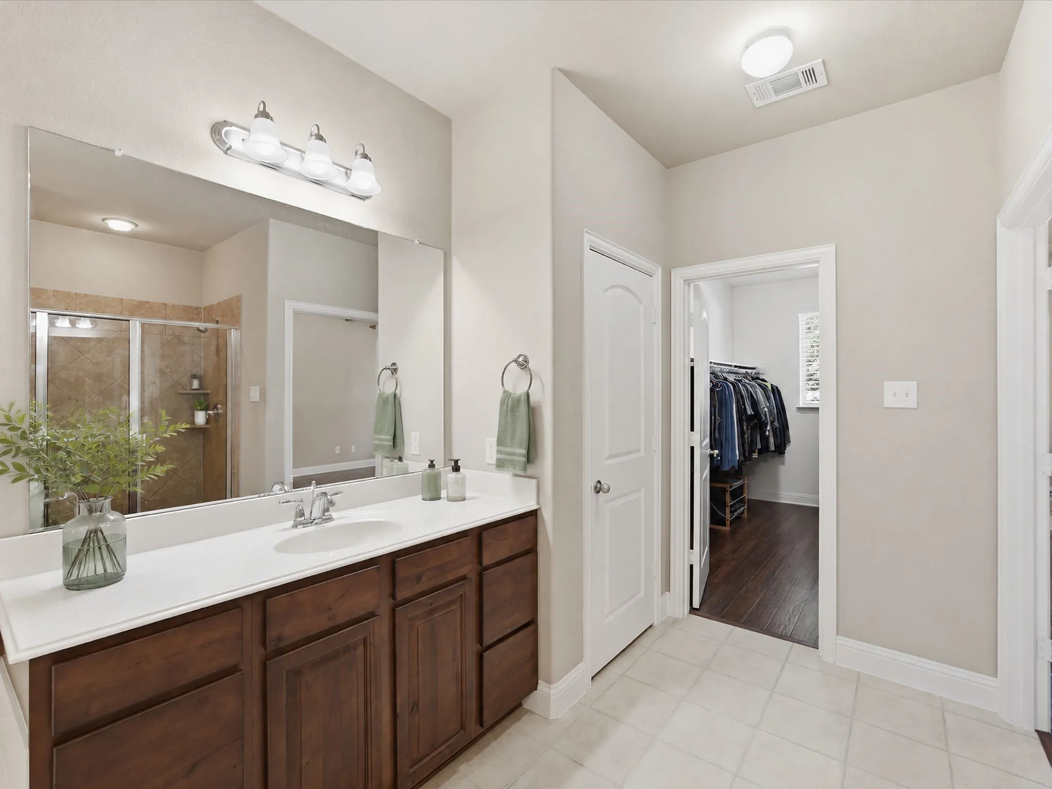 Dual-sink vanity with wood-finish cabinetry, a large frameless mirror, and overhead lighting
