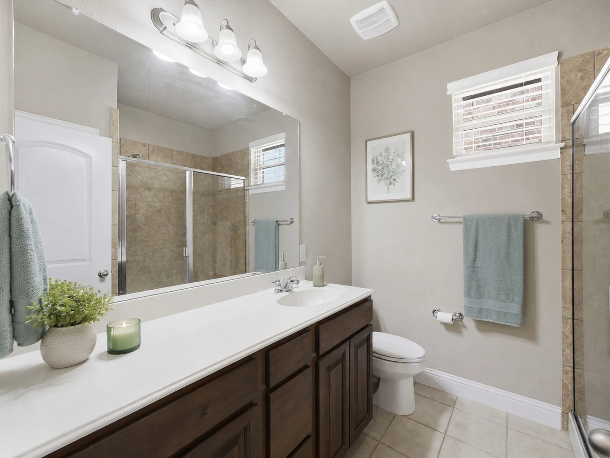 Bathroom featuring a wood-finish vanity with a white countertop, large wall mirror, and tile flooring