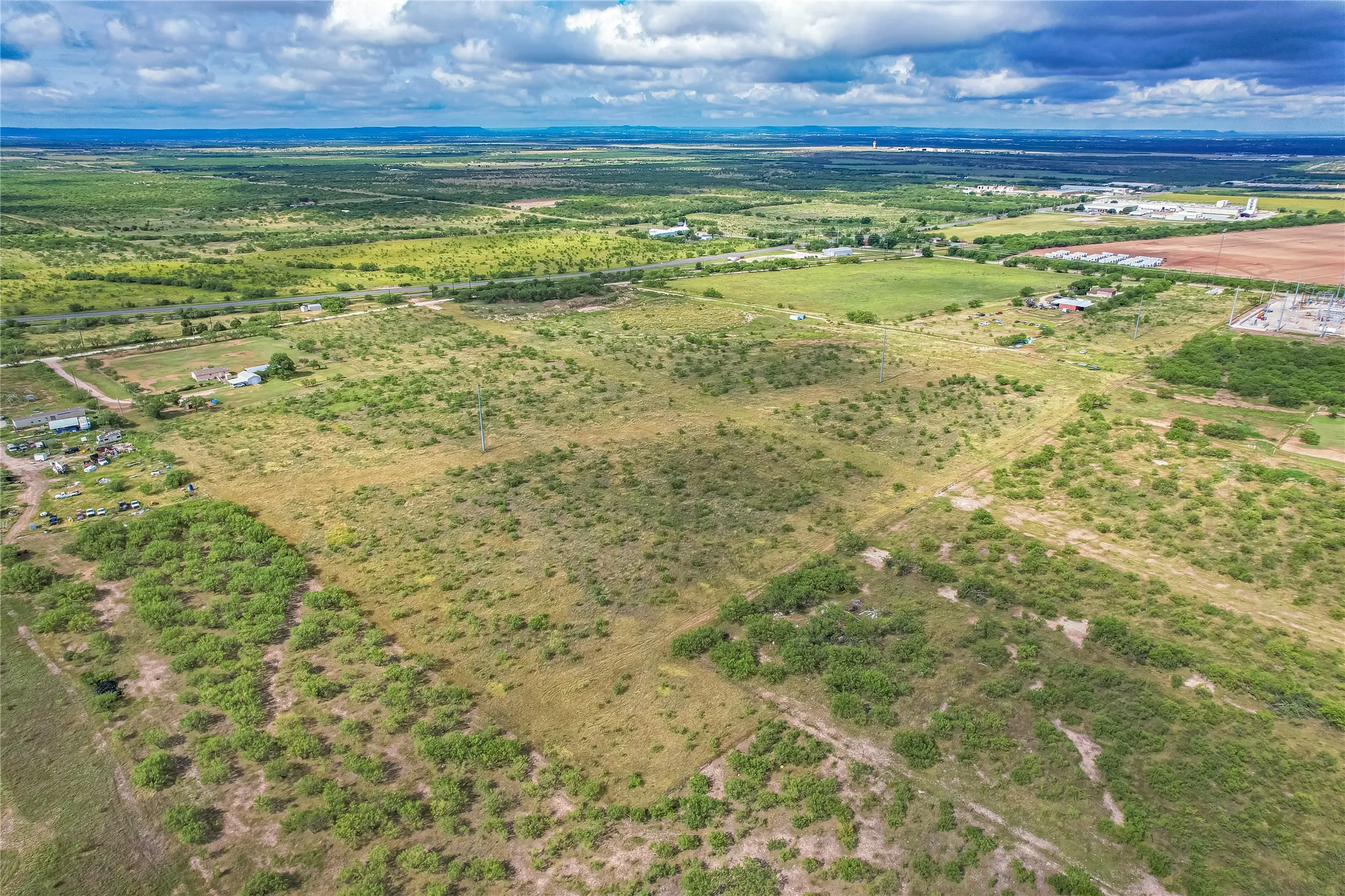 Expansive open land featuring diverse vegetation and distant infrastructure