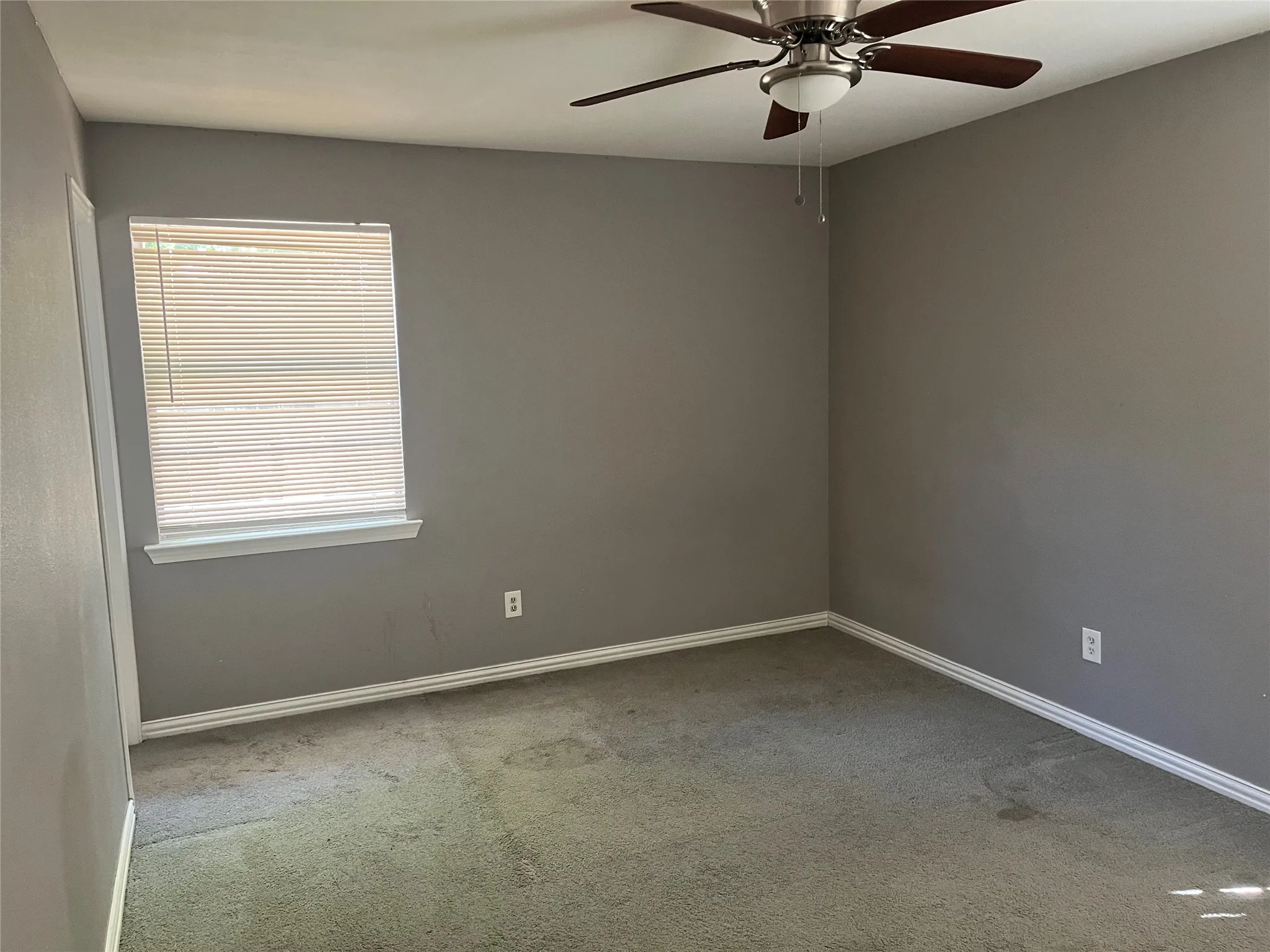 Neutral gray wall paint with white trim, a single window with horizontal blinds, and a ceiling fan with light fixture