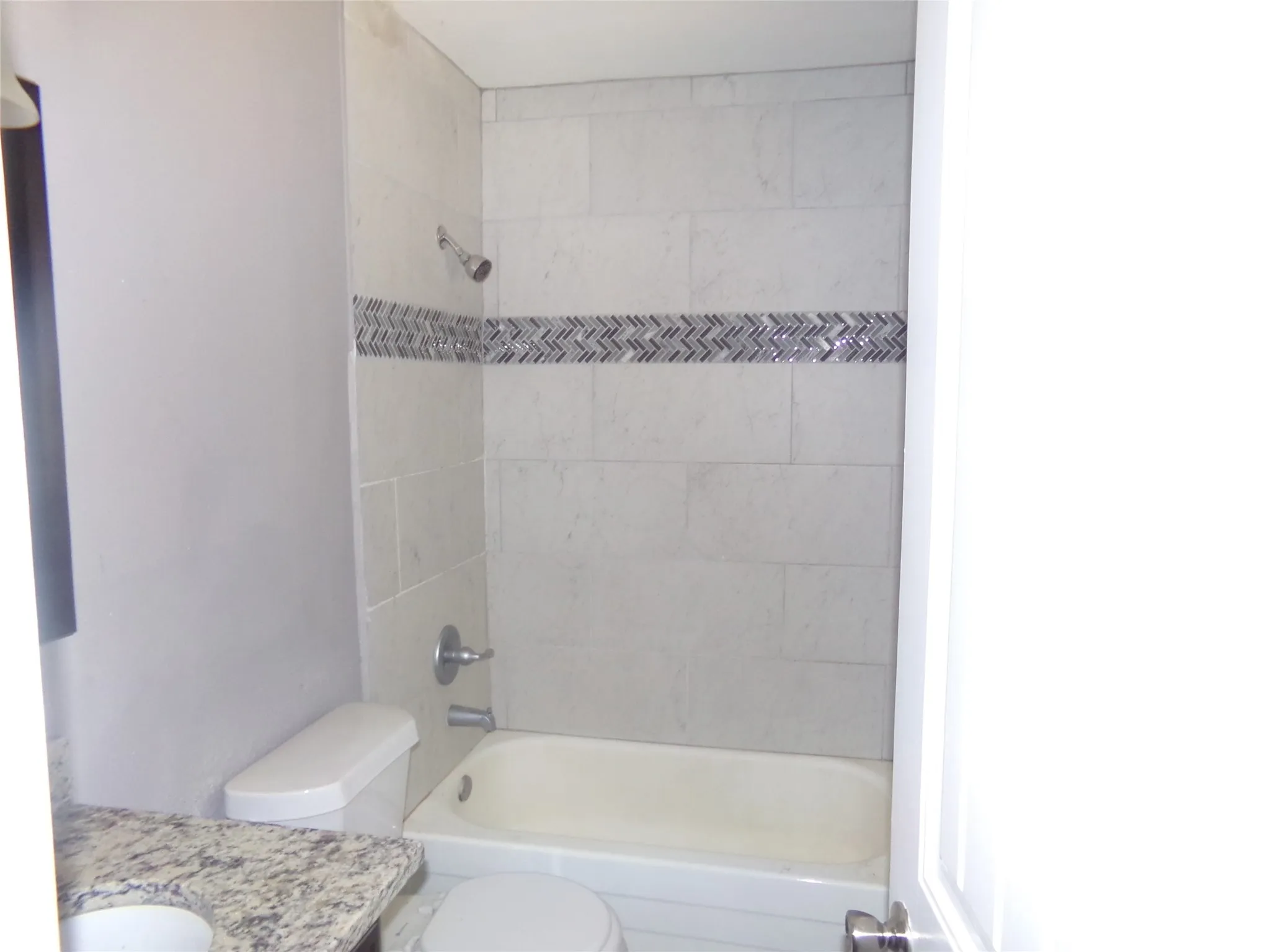 Bathtub with light-toned wall tiling, decorative mosaic accent band, and chrome fixtures
