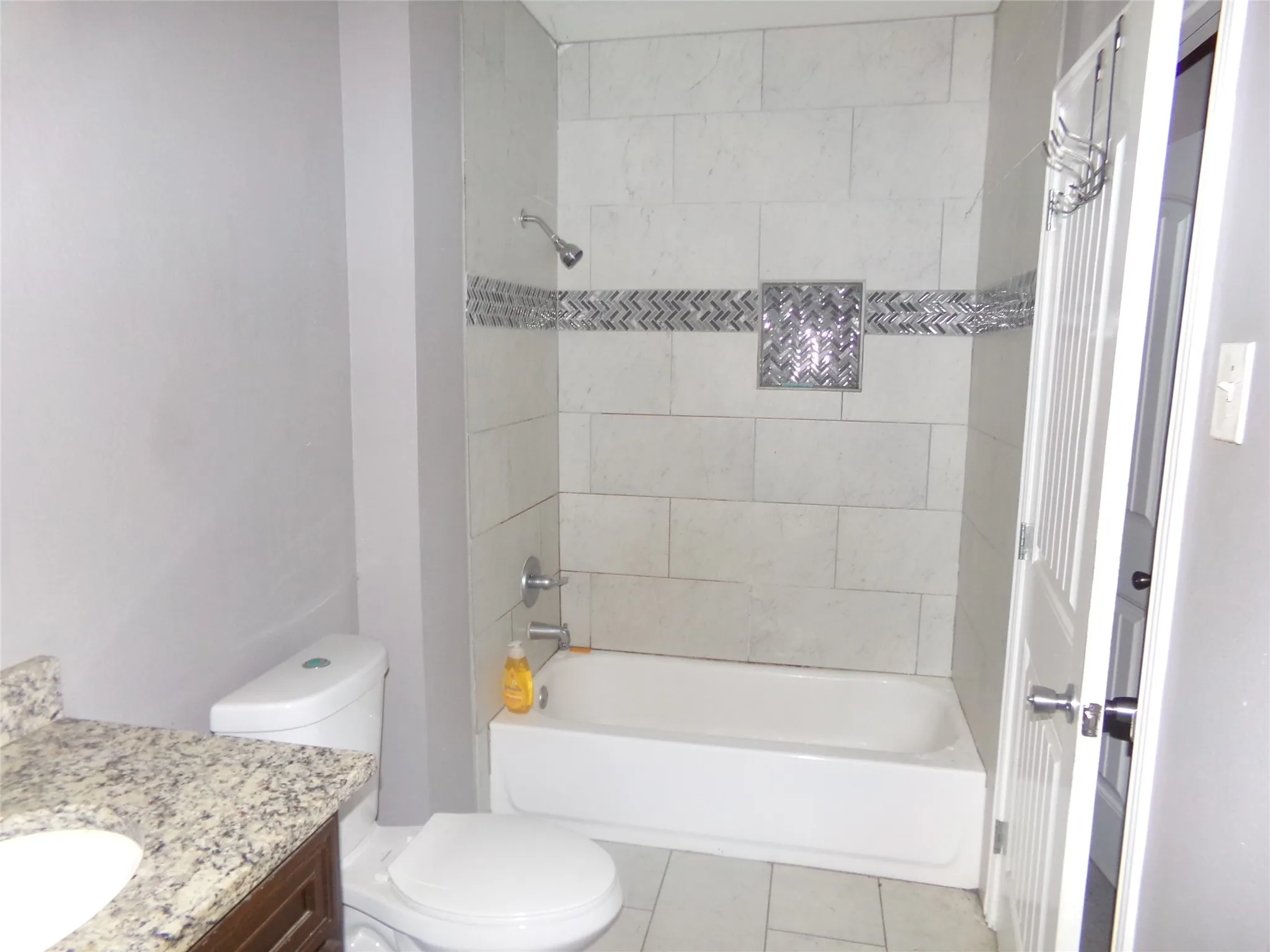 Bathroom featuring a tiled shower surround with decorative accent, built-in shower niche, white bathtub, wood-finish vanity with granite countertop, and tile flooring
