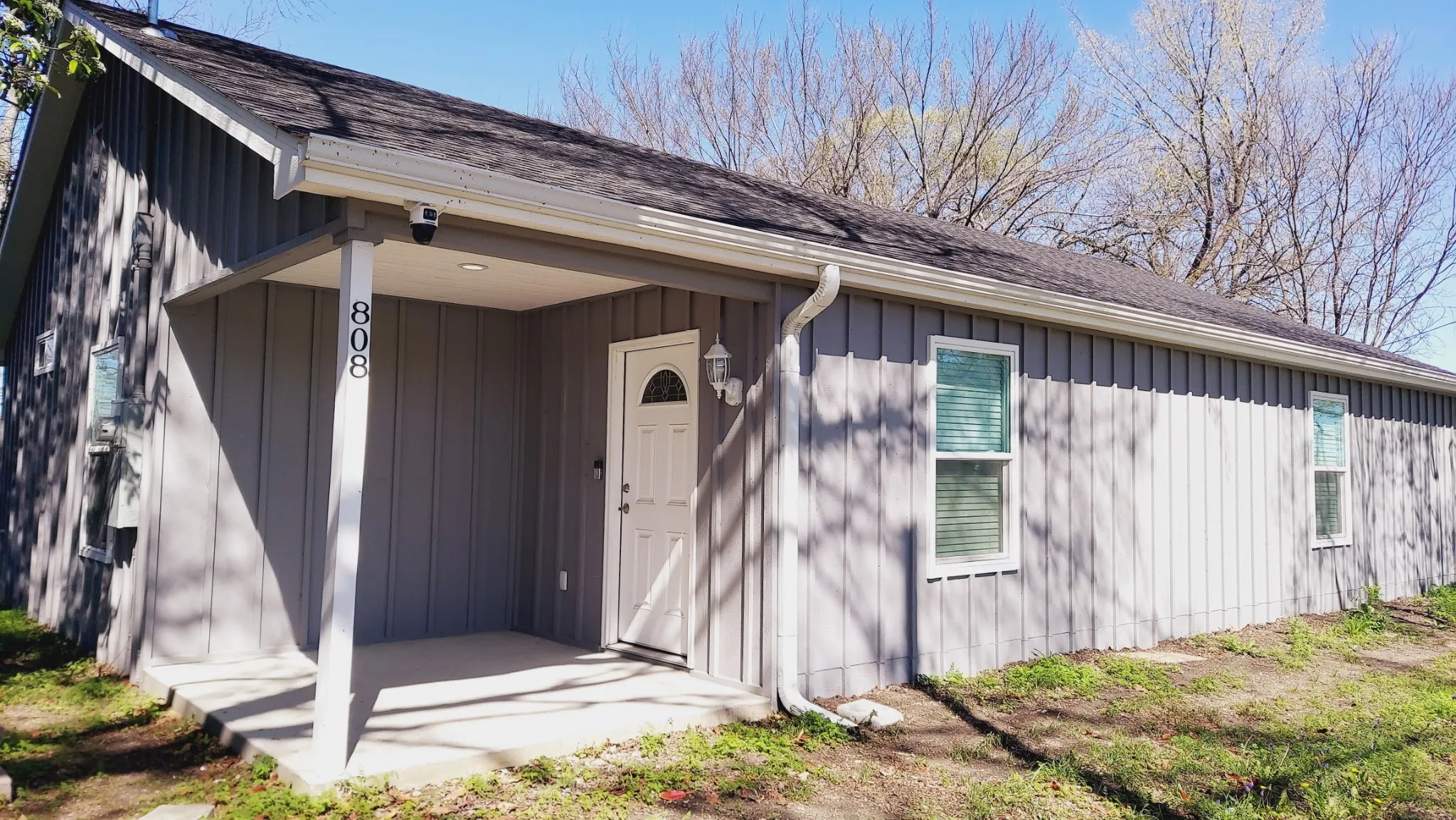 Board and batten siding, covered entry, asphalt shingle roof, white trim windows, and a white front door