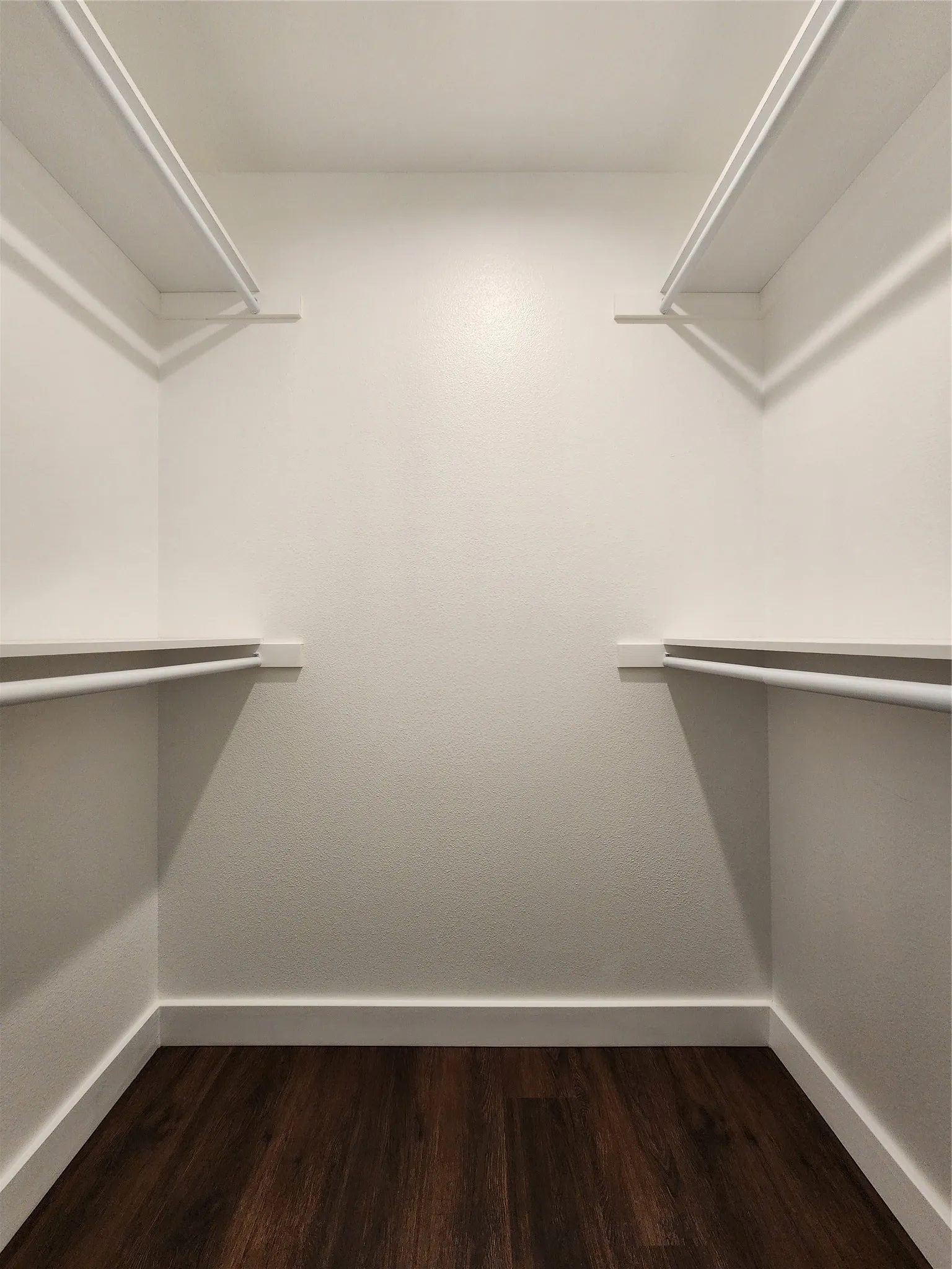 Wood-finish flooring with white walls and built-in closet shelving and hanging rods in primary closet.
