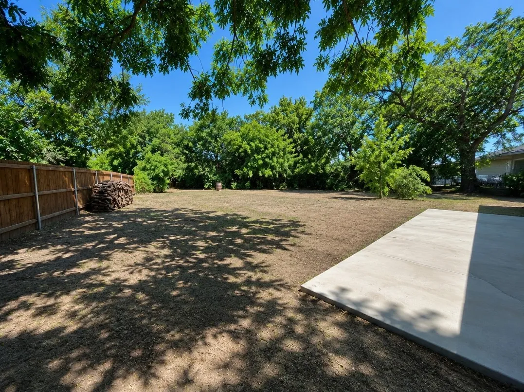 Expansive backyard featuring a privacy fence, mature trees, and a concrete patio