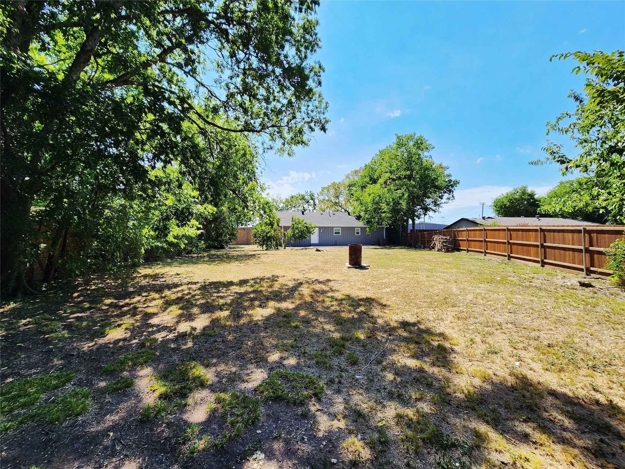 Expansive backyard featuring a wood fence, mature trees, and a visible portion of the property structure