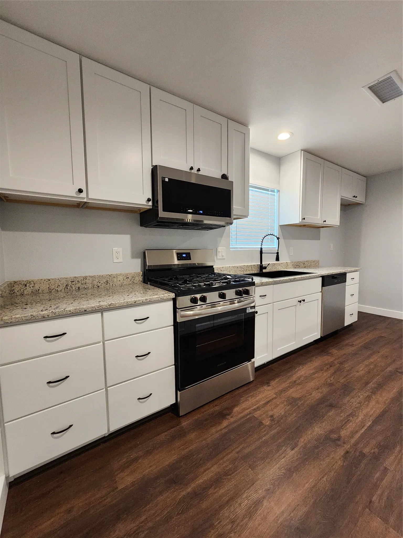 White shaker-style cabinetry, stainless steel appliances, granite-look countertops, black faucet, and wood-finish flooring