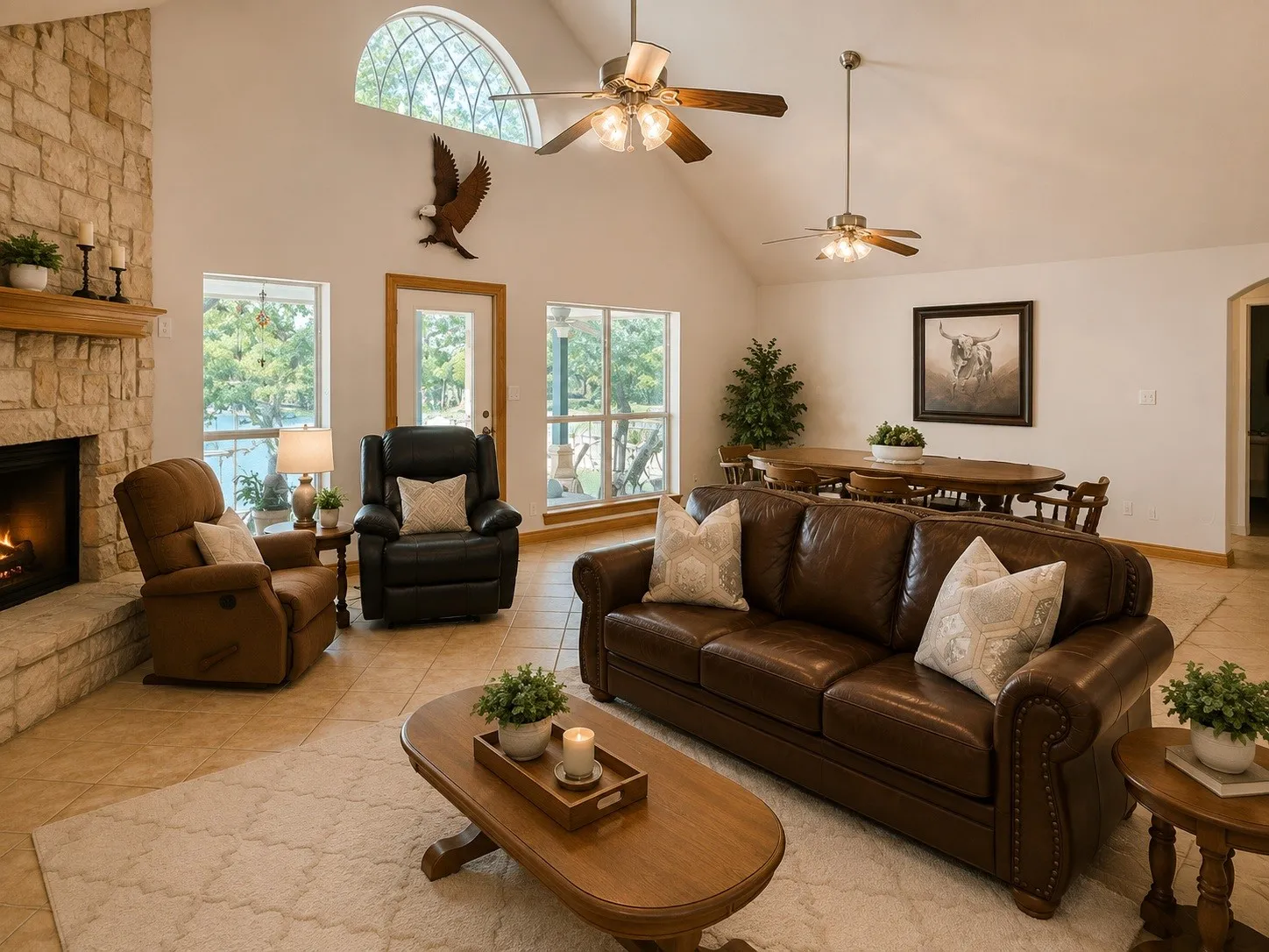 Vaulted ceilings with multiple ceiling fans, stone-clad fireplace with wood mantle, arched transom window, large windows with exterior access, and tile flooring