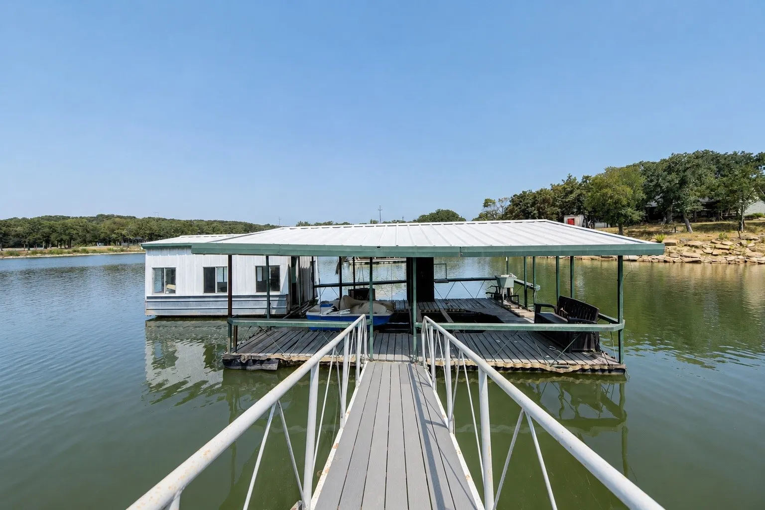 Houseboat with a covered deck, white siding, and multiple windows