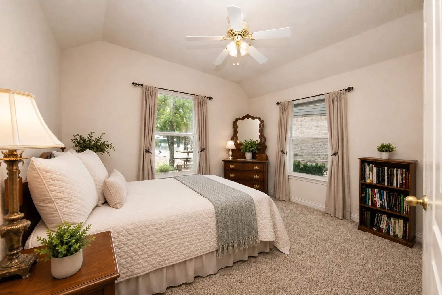 Vaulted ceiling with a ceiling fan, carpeted flooring, two windows with drapes, and a built-in wooden bookcase