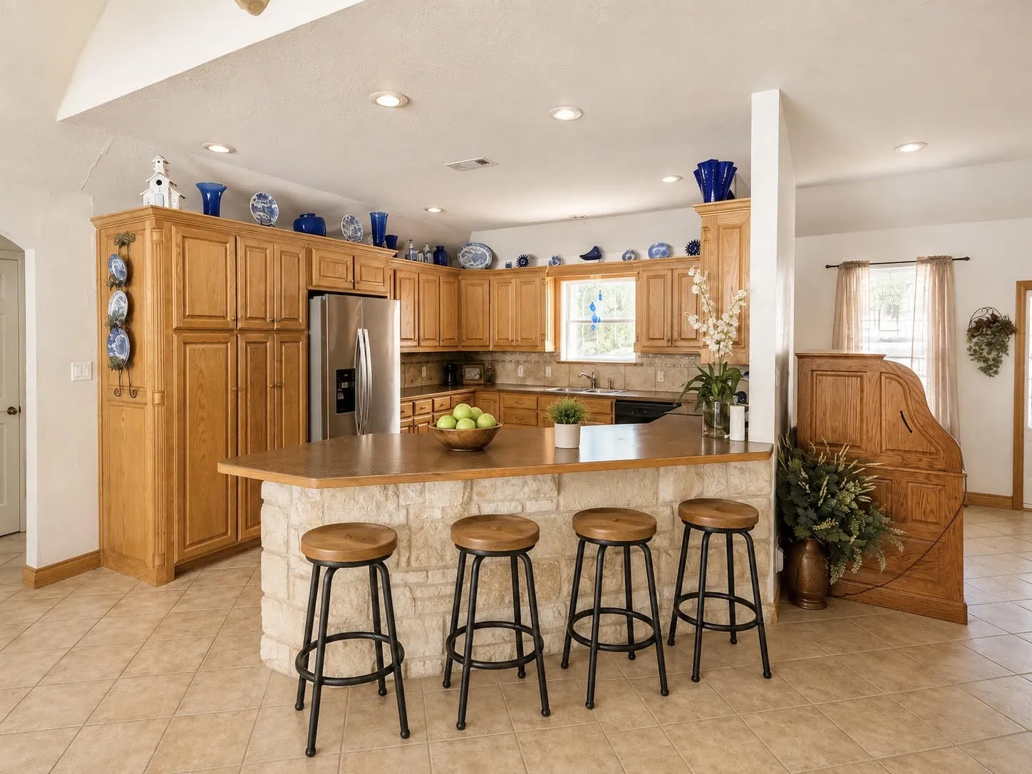 Kitchen featuring a stone-clad island, extensive wood cabinetry, stainless steel refrigerator, and recessed lighting