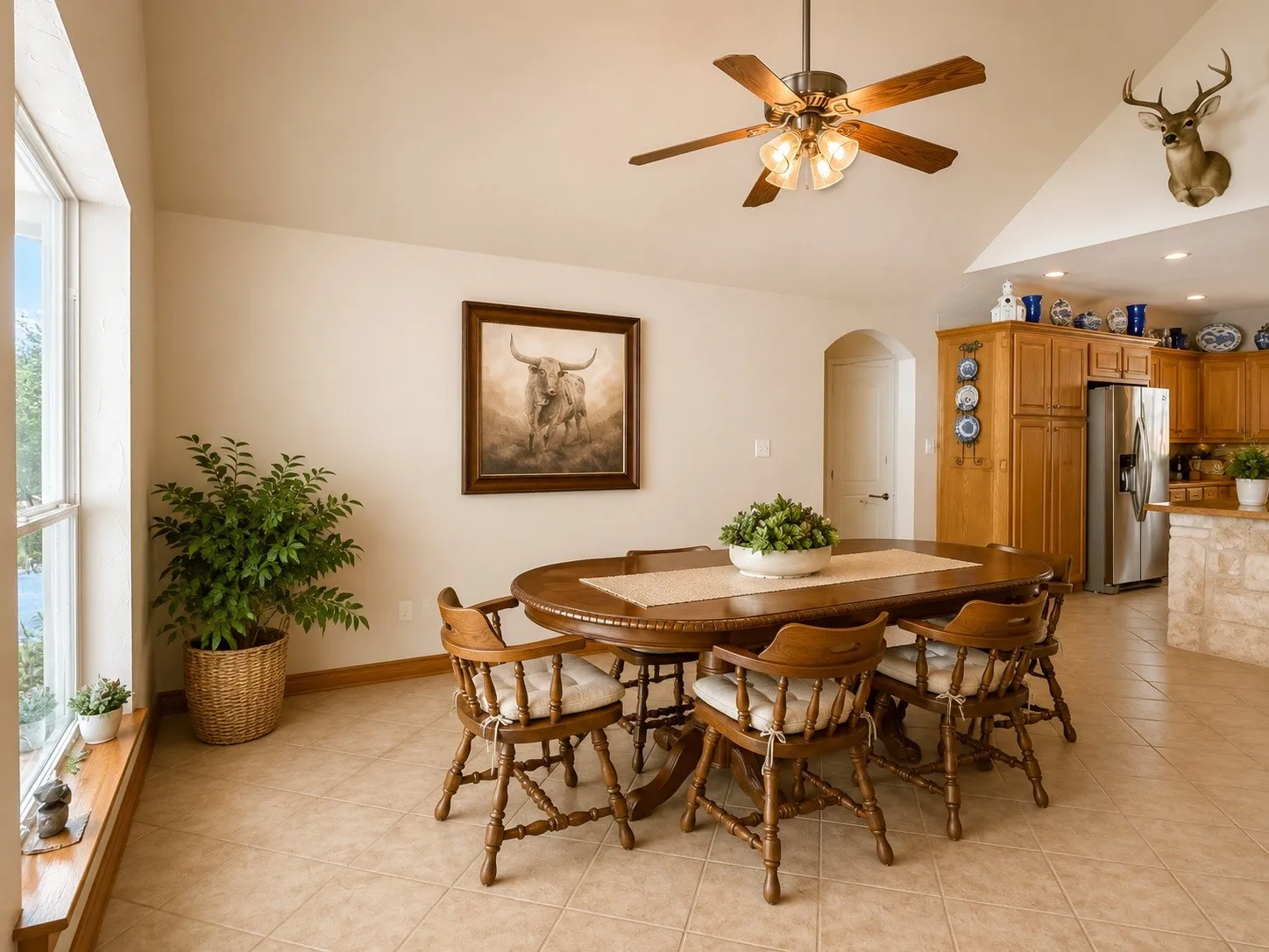 Vaulted ceiling, ceiling fan with integrated lighting, tiled flooring, wood cabinetry, and a large window