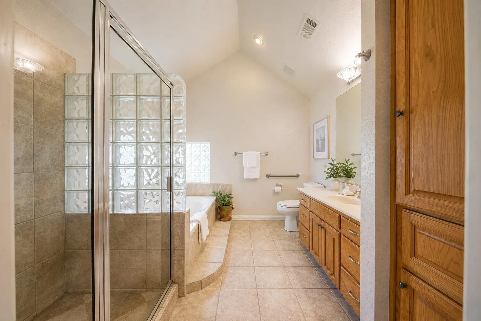 Vaulted ceiling, tiled flooring, glass-enclosed shower, built-in bathtub with tiled surround, and a double vanity with wood-finish cabinetry