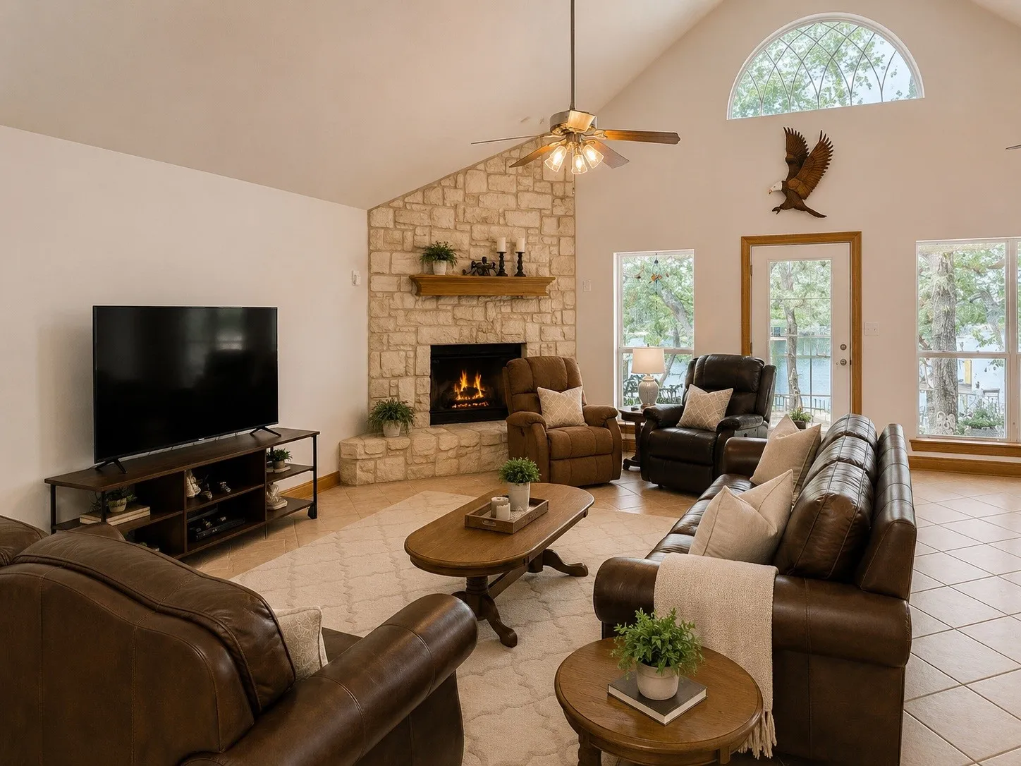 Vaulted ceiling, stone-clad fireplace, arched transom window, ceiling fan, and tile flooring