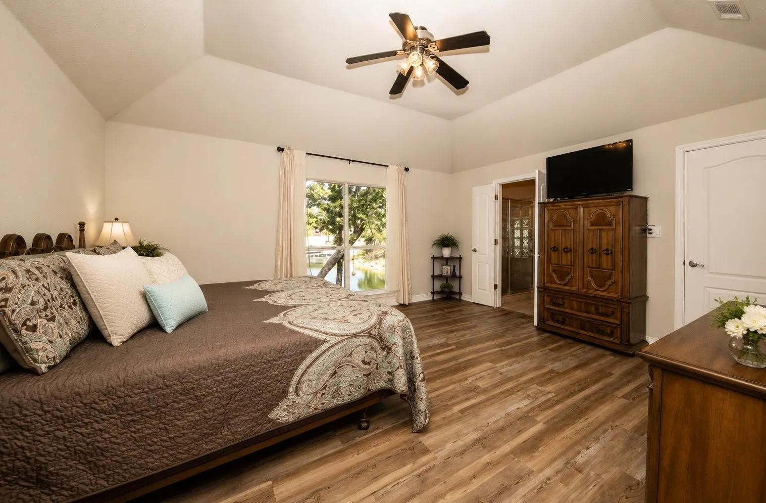 Vaulted ceiling with a ceiling fan, wood-finish flooring, and a large window with outdoor scenery