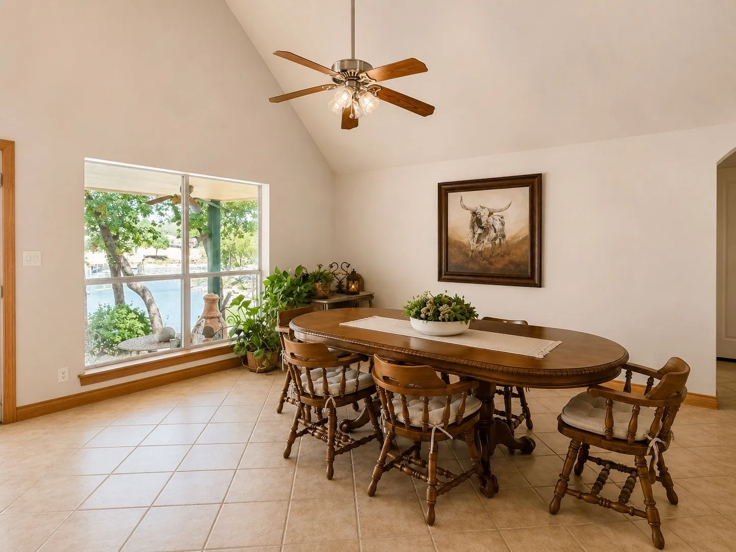Vaulted ceiling with a ceiling fan, large window, tile flooring, and light-colored walls