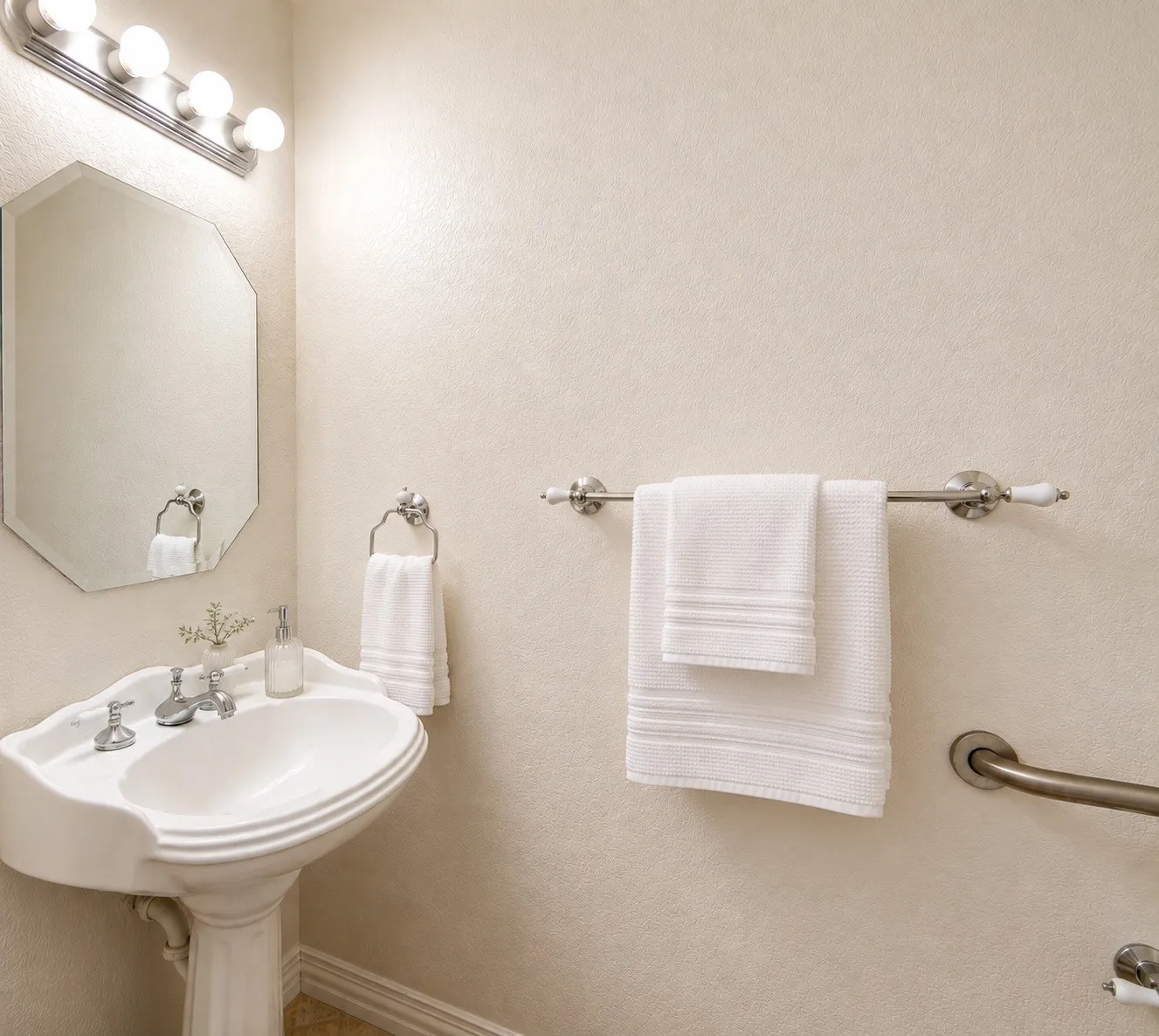 Pedestal sink with chrome fixtures, octagonal wall mirror, and vanity lighting