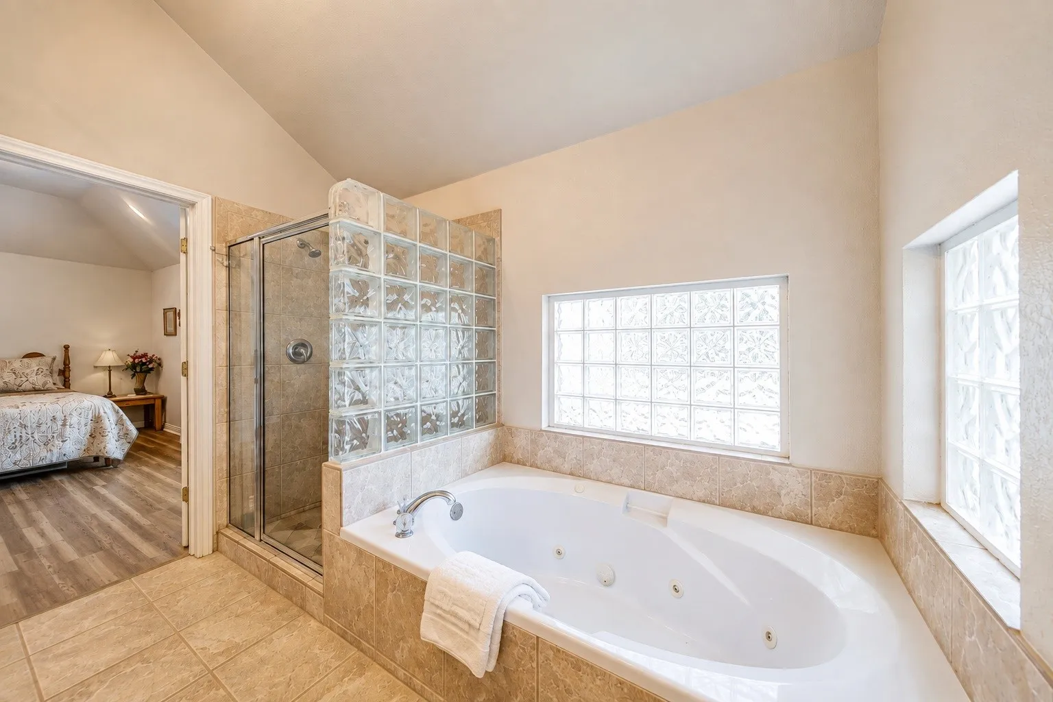 Soaking tub with integrated jets, glass block windows, tiled shower enclosure with a glass door, and tiled flooring