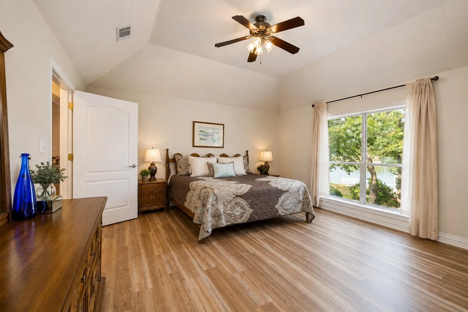 Vaulted ceiling with a ceiling fan, wood-finish flooring, and a large window