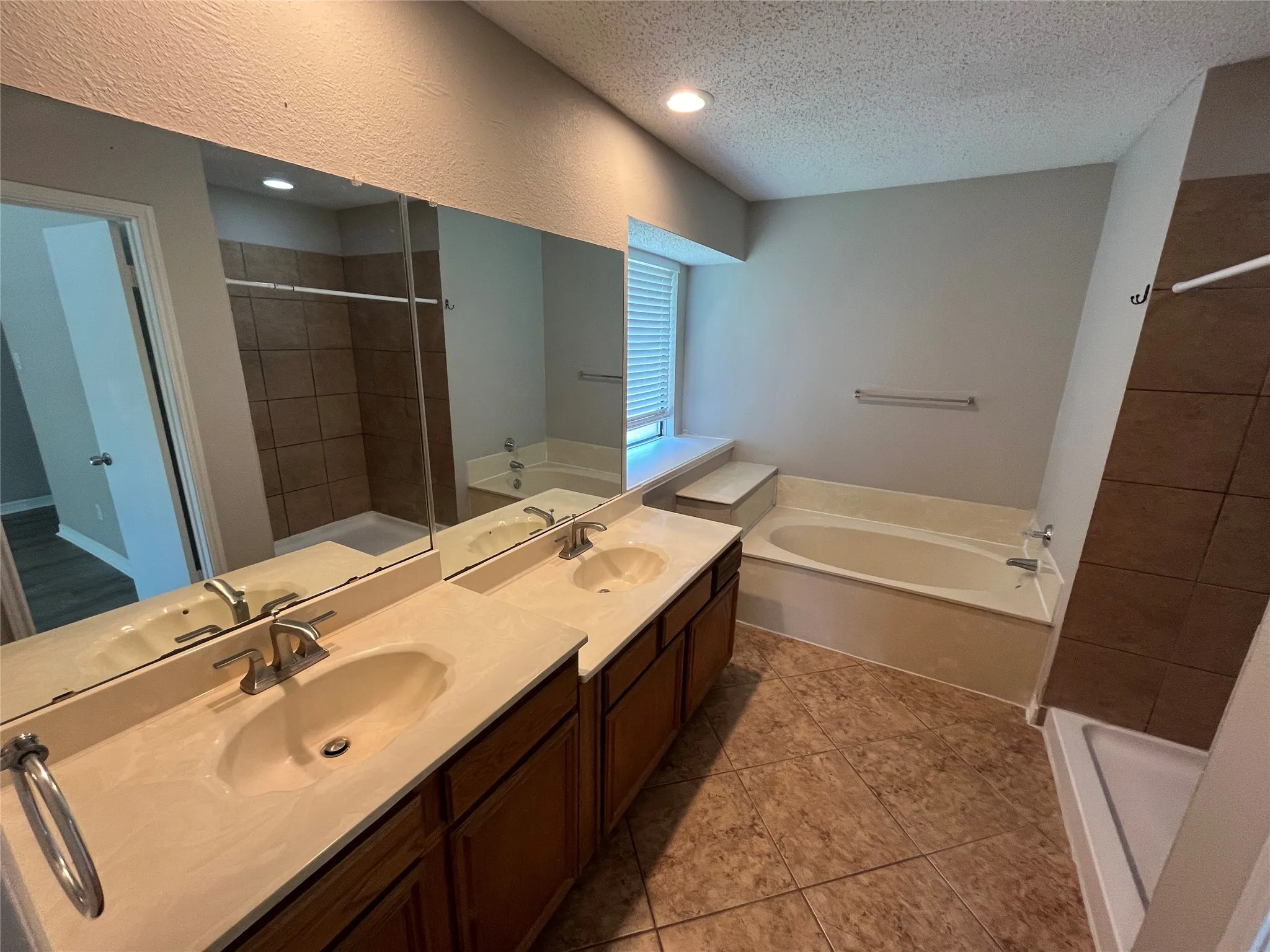 Dual vanity with integrated sinks and brushed nickel fixtures, large mirror, recessed lighting, tile flooring, and a built-in bathtub