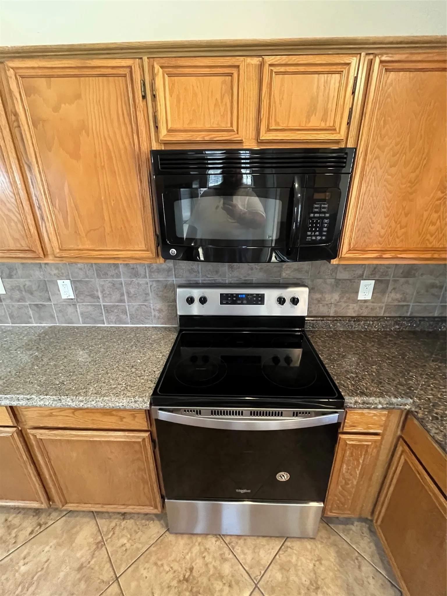 Stainless steel and black range, coordinating over-the-range microwave, granite-look countertops, subway tile backsplash, and light wood-finish cabinetry