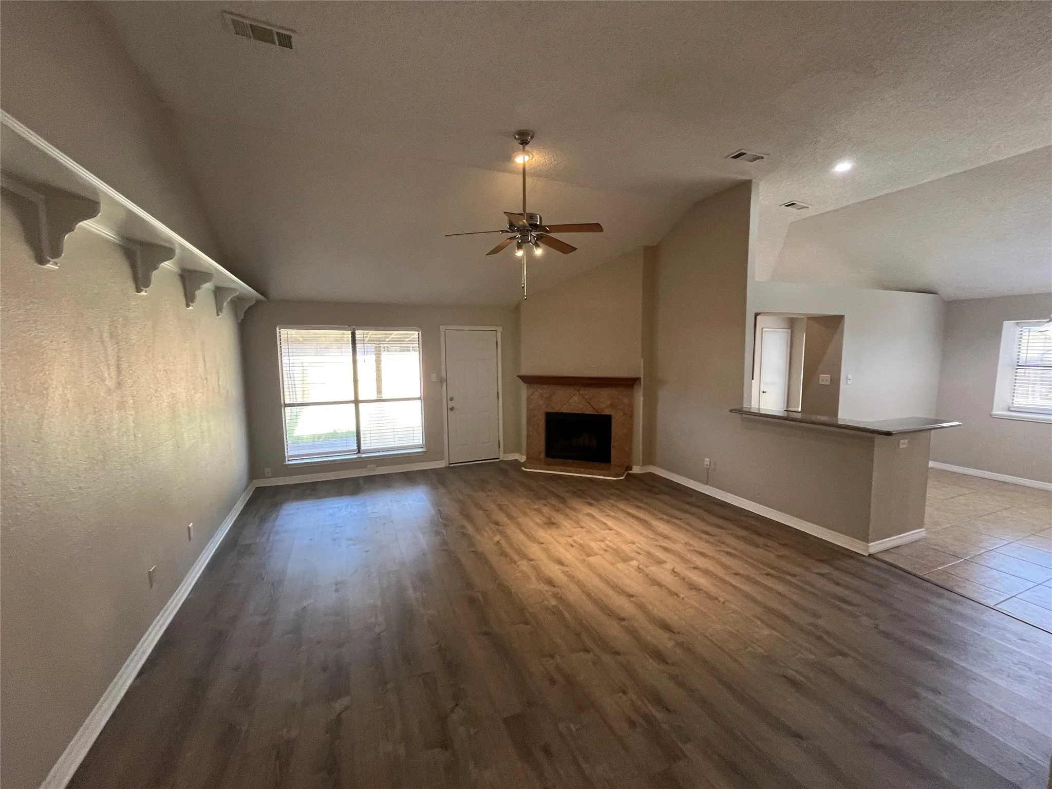 Spacious living area featuring wood-finish flooring, a fireplace with a tile surround and wood mantle, and an integrated breakfast bar with a dark countertop