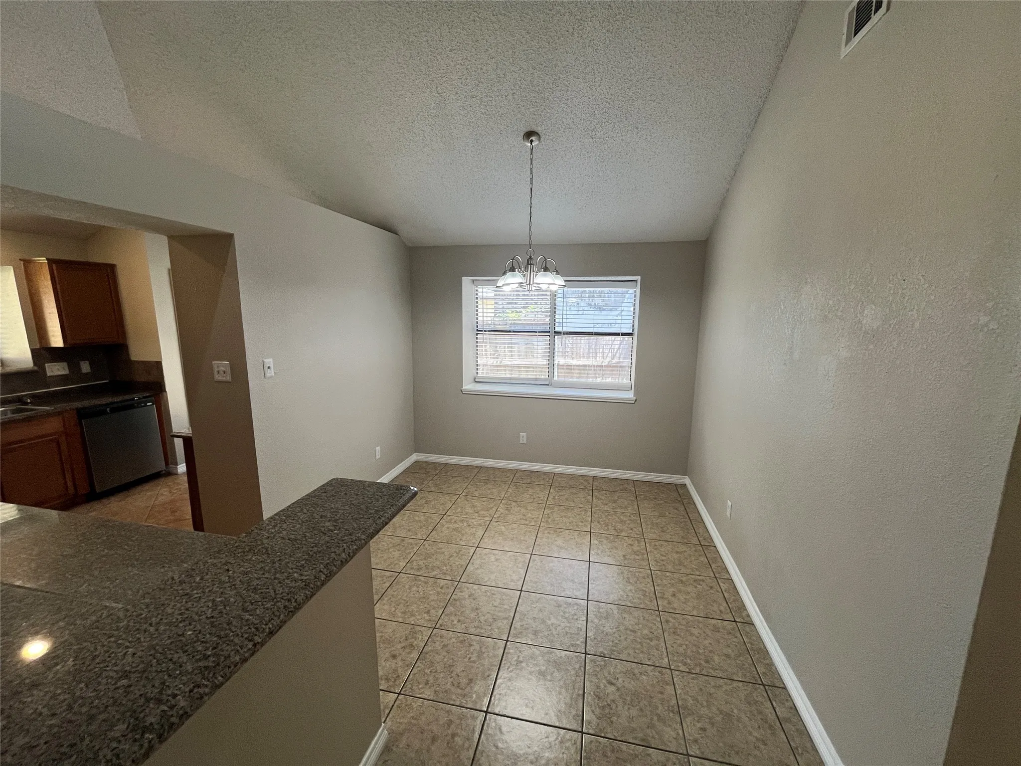Tile flooring with a neutral finish, a single window with blinds, and a built-in breakfast bar with a granite-finish countertop