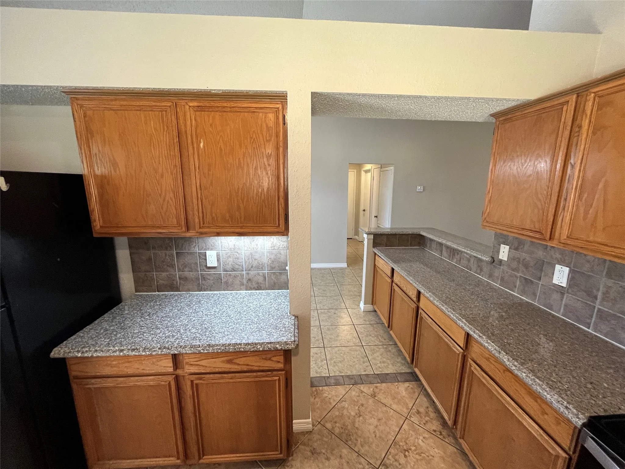 Wood-finish cabinetry, speckled countertops, tile backsplash, and tile flooring