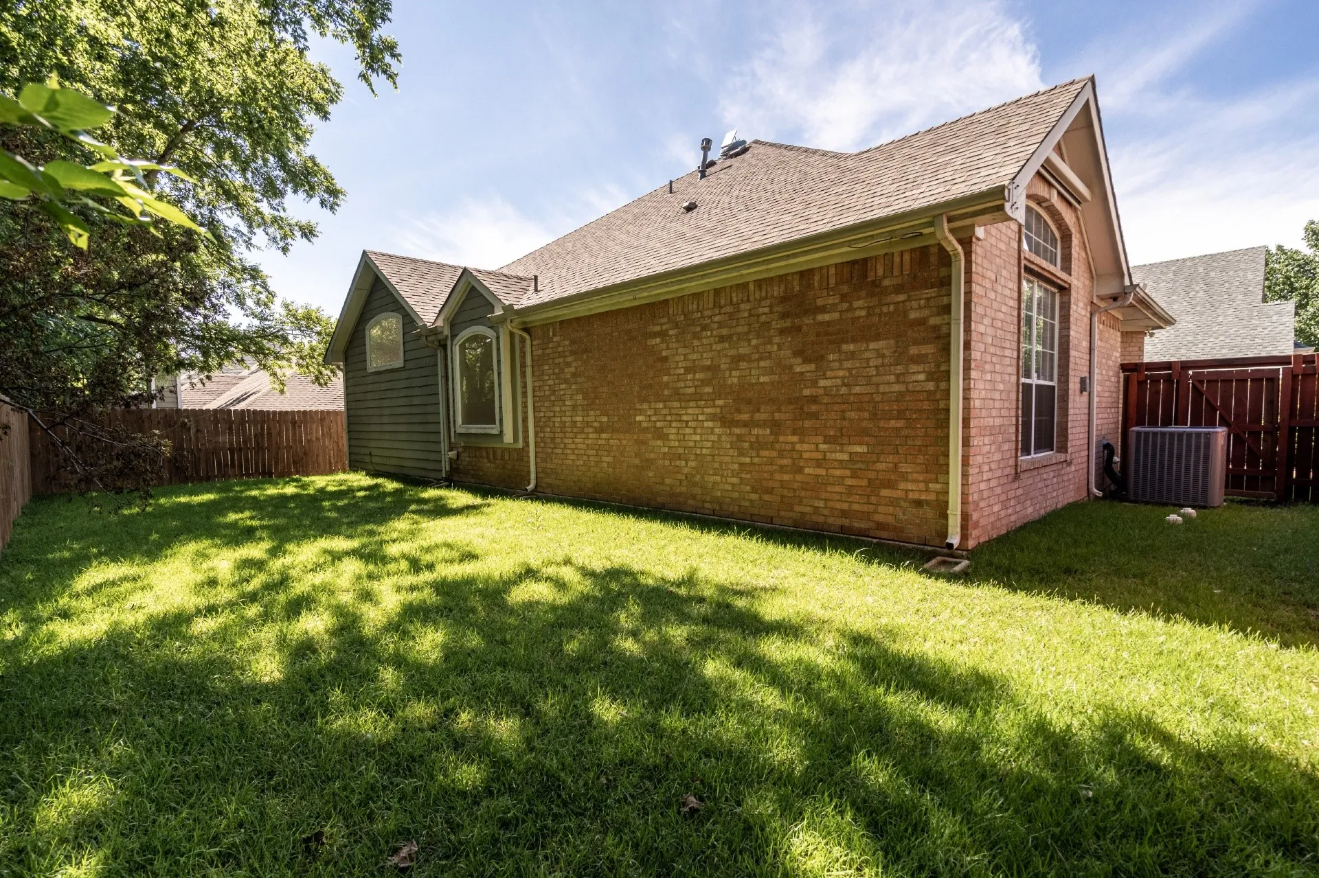 Exterior brick siding, gabled roofline, arched windows, and a wood privacy fence