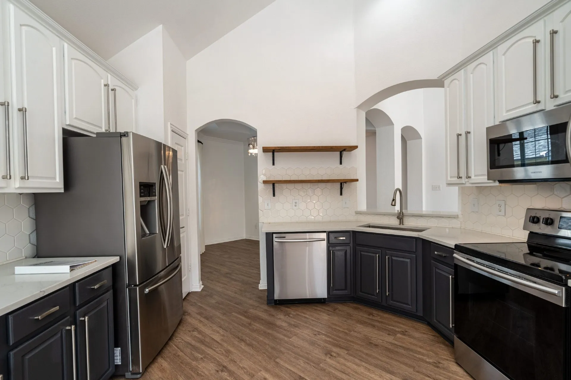 Vaulted ceiling kitchen featuring stainless steel appliances, two-tone cabinetry, hexagon tile backsplash, and wood-finish flooring