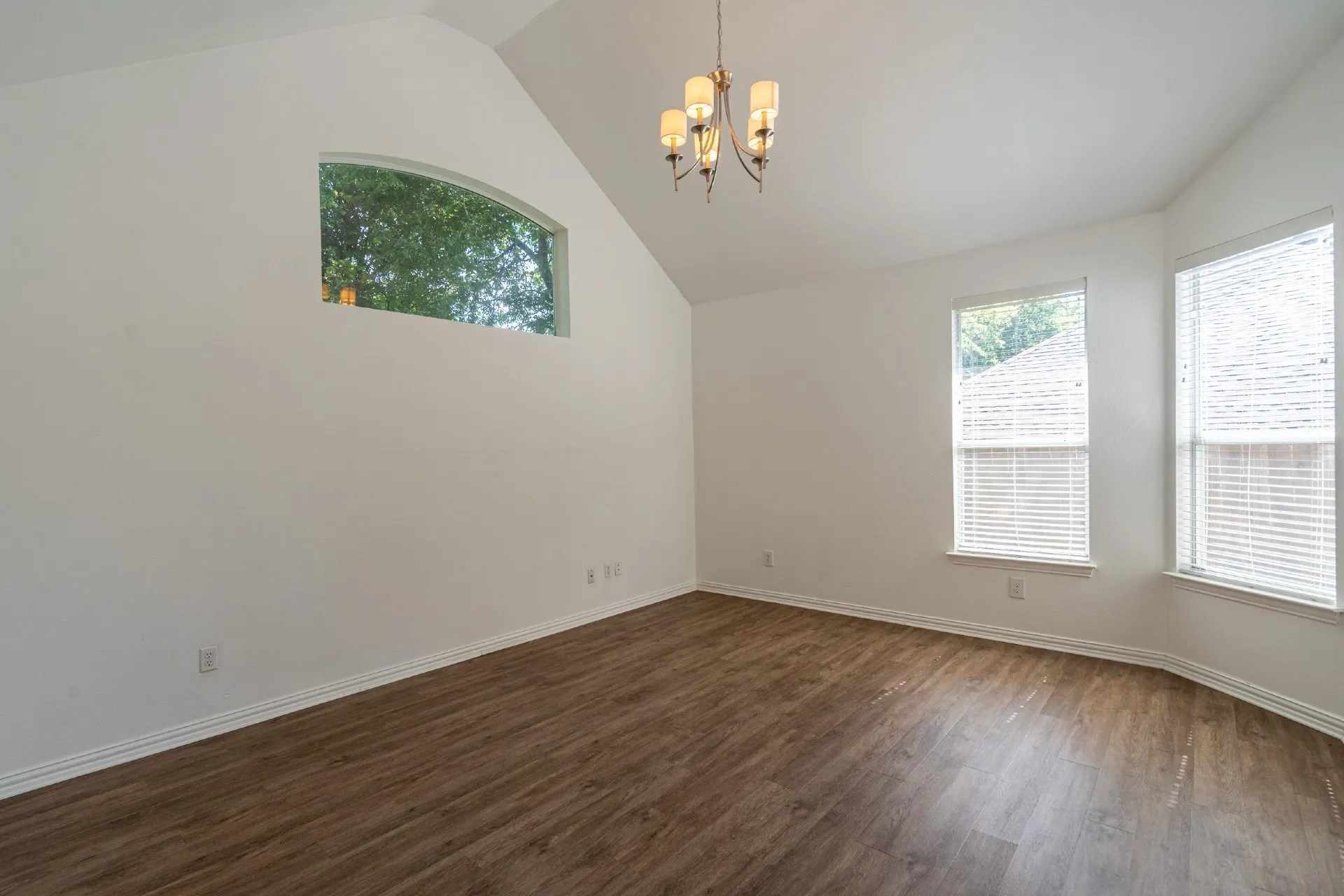Vaulted ceiling featuring a chandelier, wood-finish flooring, and multiple windows with blinds