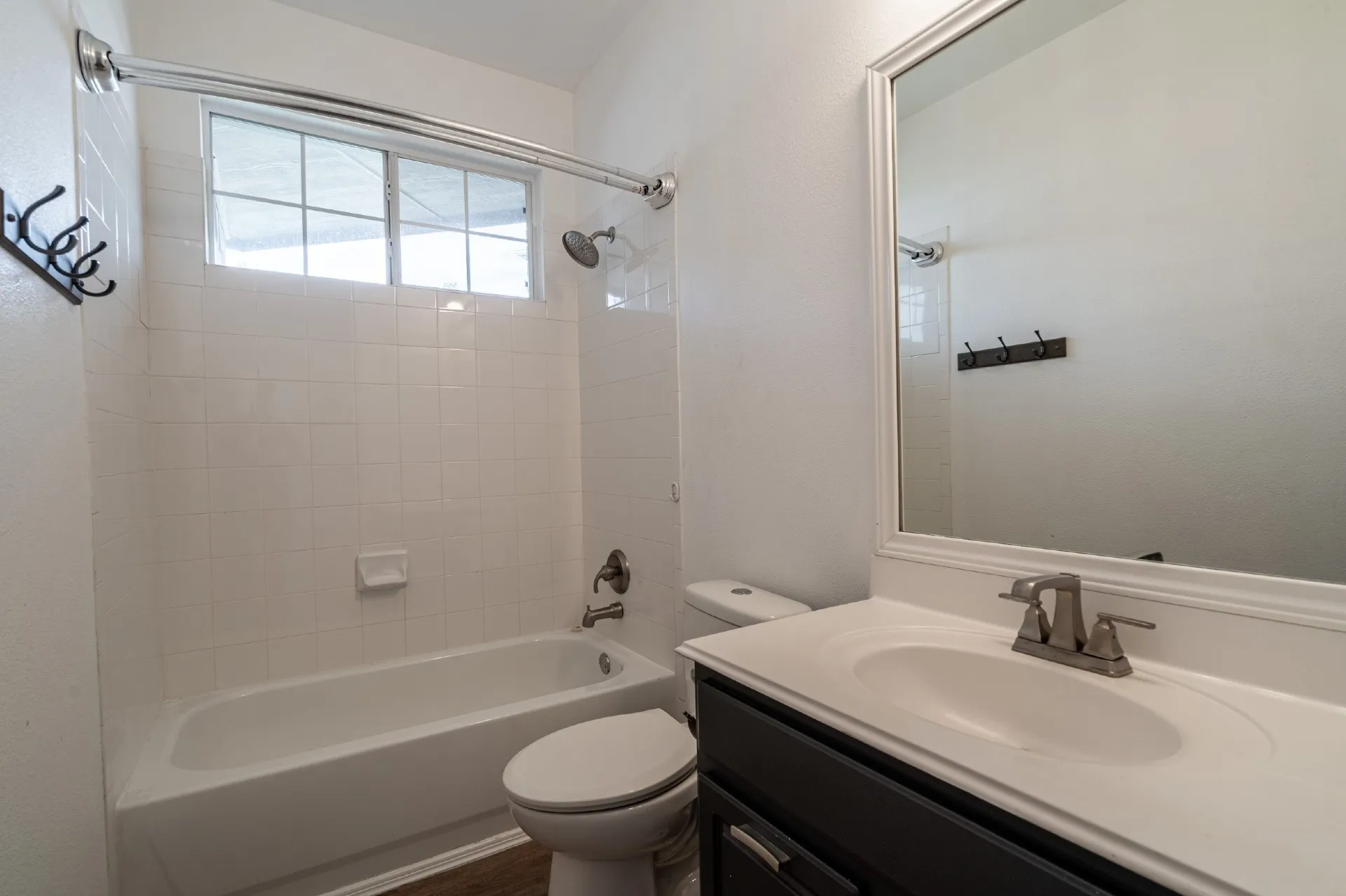 Bathroom featuring a white bathtub, ceramic tile surround, window with grid, dark-toned vanity with a white countertop and integrated sink, and a framed mirror
