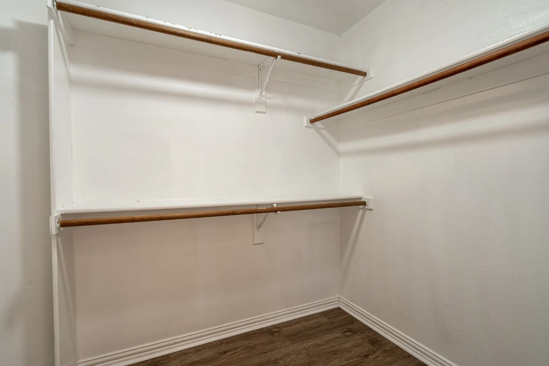 White-painted closet with wood-finish flooring, multiple shelving units, and integrated hanging rods